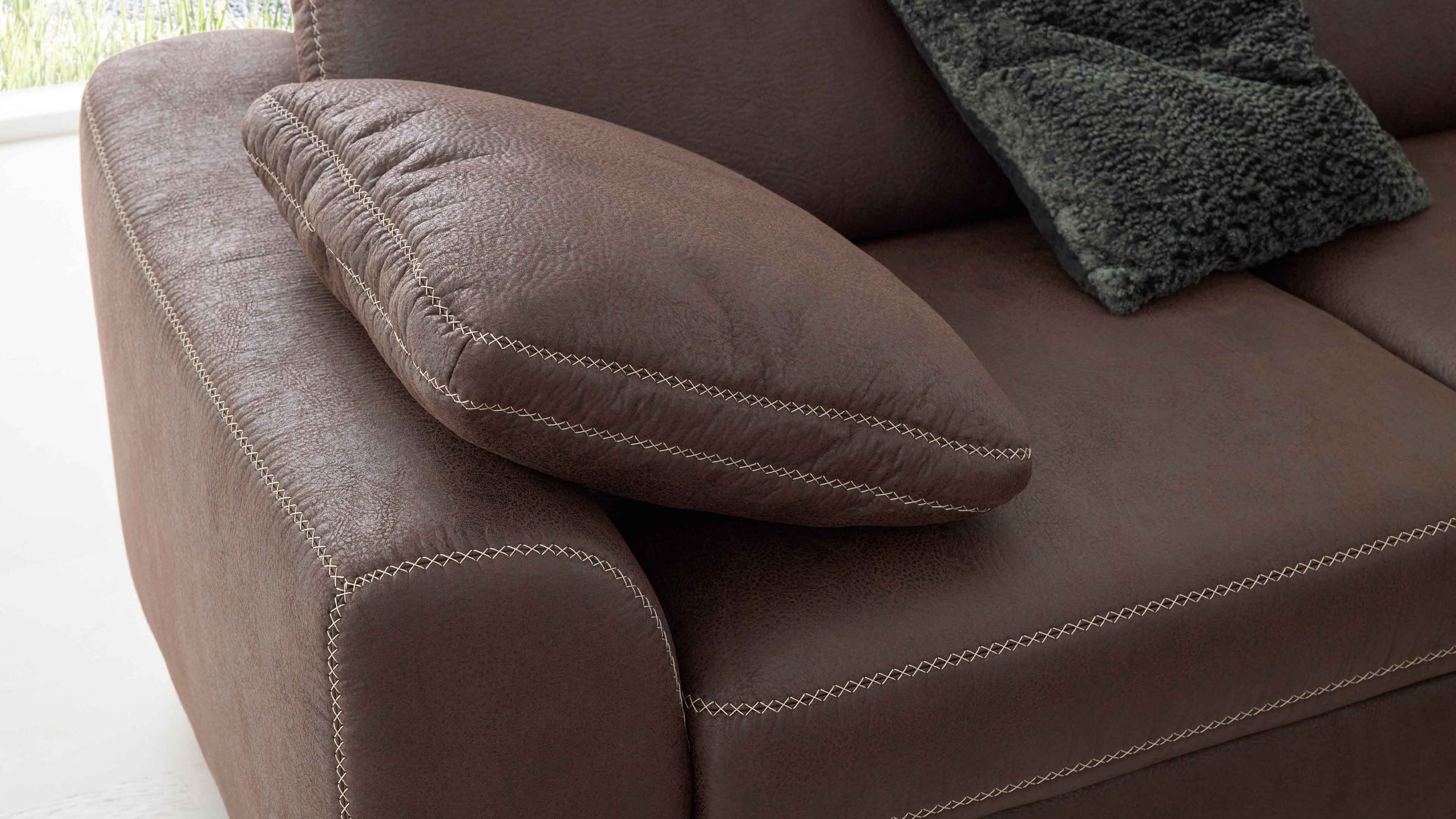 Braunes Armlehnkissen mit sichtbaren hellen Nähten auf braunem Sofa mit weiteren Kissen