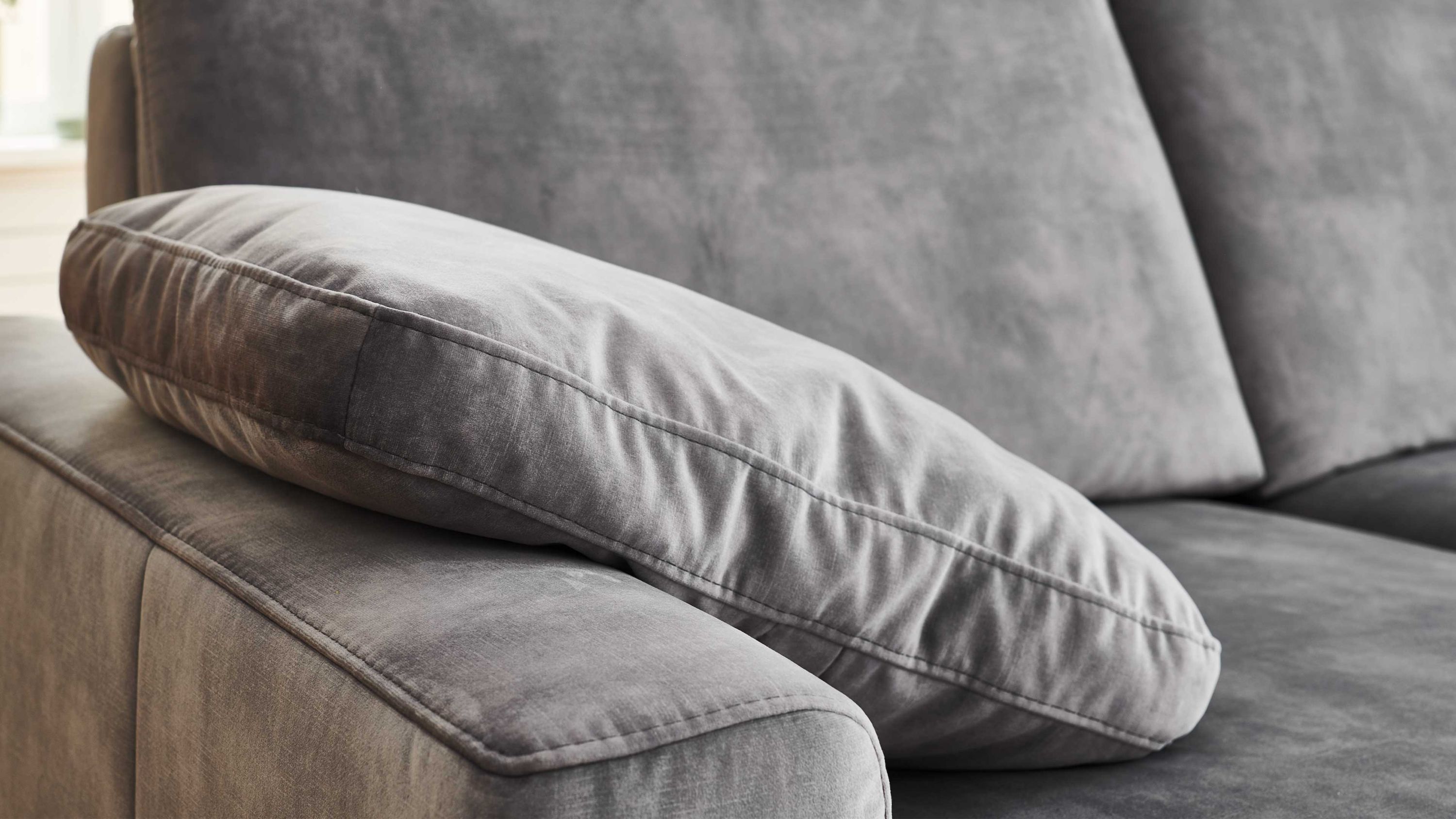 Rechteckiges silberfarbenes Kissen auf der Armlehne eines grauen Sofas
