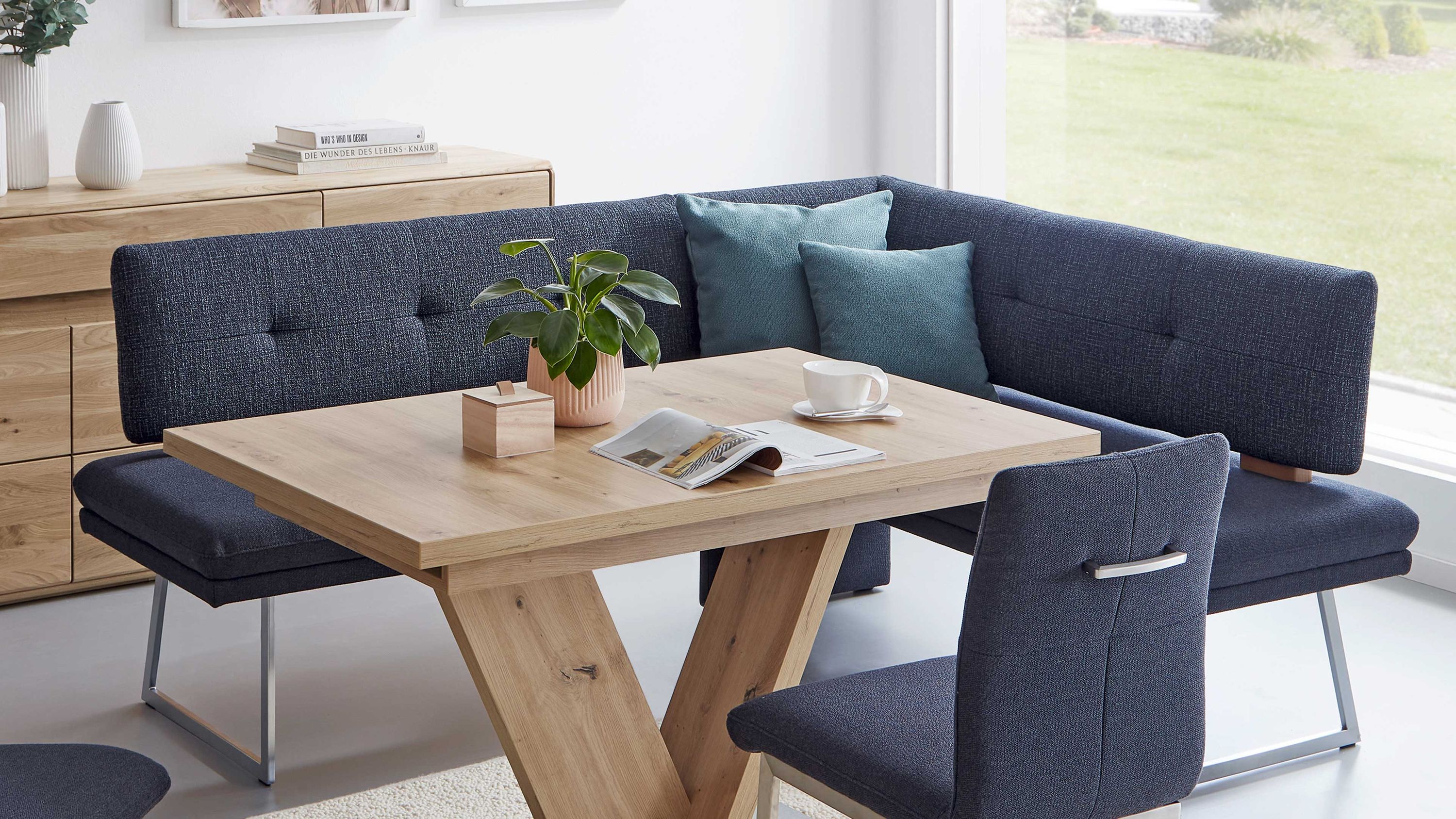 Eckbank mit blauem Stoffbezug und Holztisch Eckbank mit blauem Stoffbezug und Edelstahlkufen rechteckiger Holztisch mit V-förmigen Beinen blauer Stuhl mit Griff