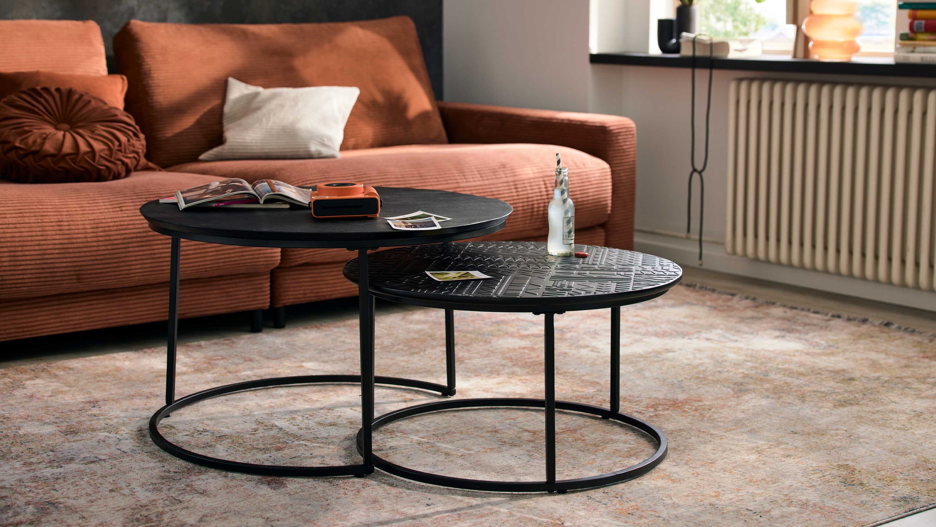 Zweiteiliges Couchtisch-Set mit zwei runden schwarzen Tischen auf Metallgestellen vor einem braunen Sofa
