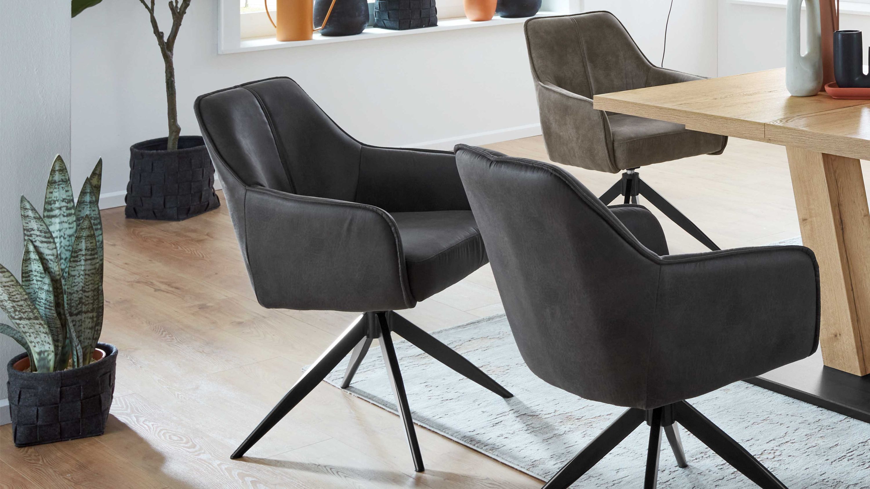 Drehbare Armlehnstühle mit Mikrofaserbezug und Metallgestell Drei drehbare Armlehnstühle mit anthrazitfarbener und brauner Mikrofaser und schwarzem Metallgestell um einen Holztisch