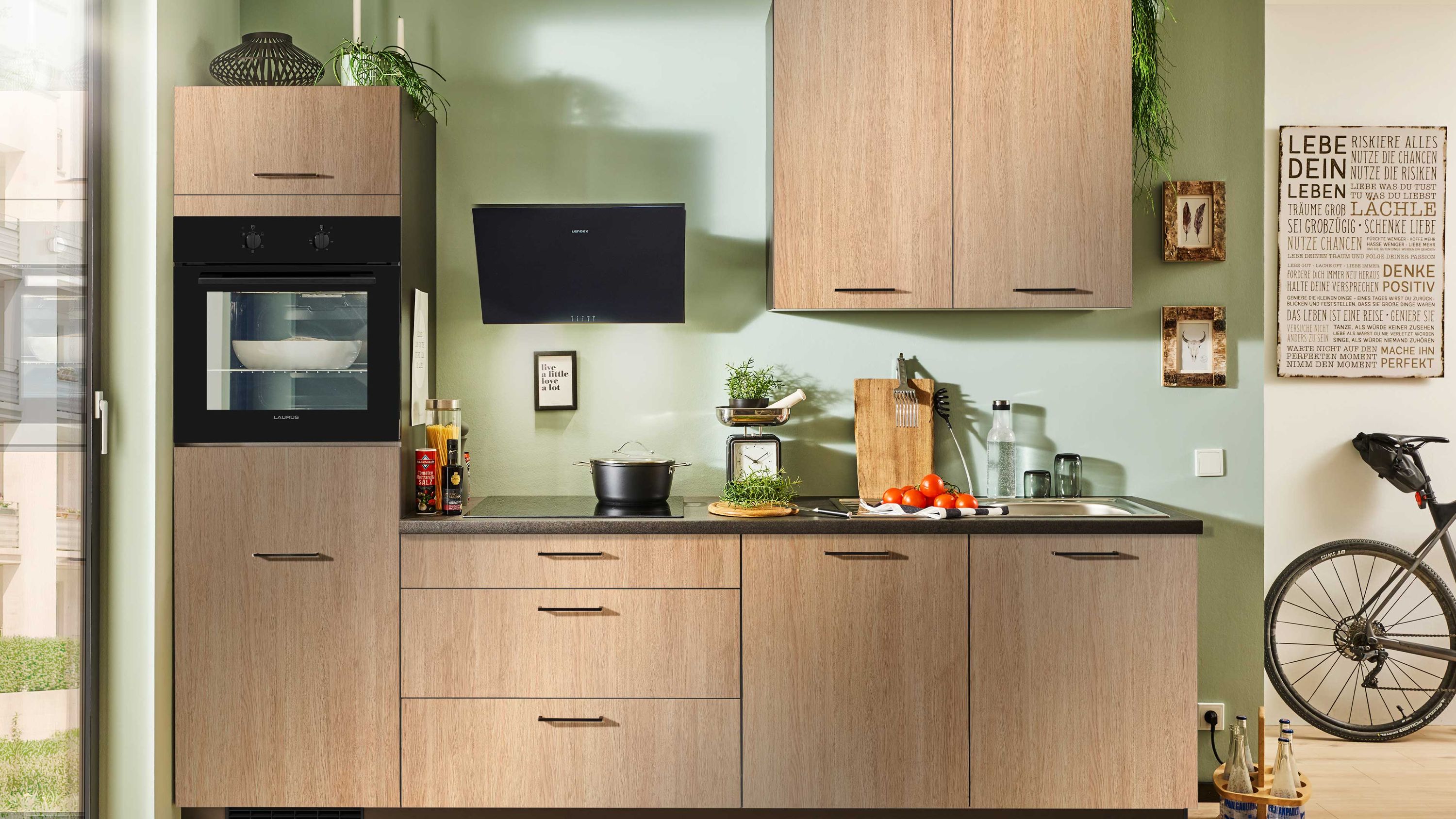 Kompakte Holzküche mit hochgebautem Backofen und grüner Wand im Hintergrund.