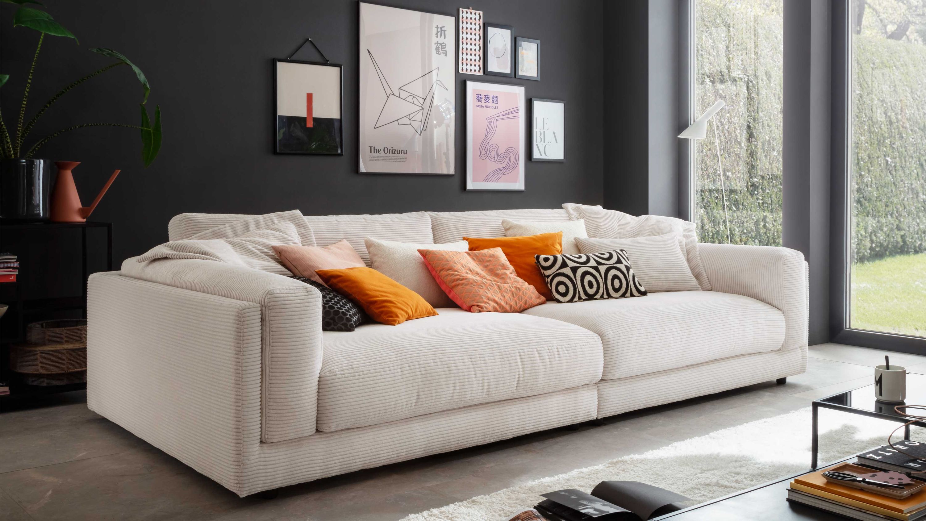 Großes weißes Sofa mit breiten Armlehnen und mehreren bunten Kissen in einem modernen Wohnzimmer