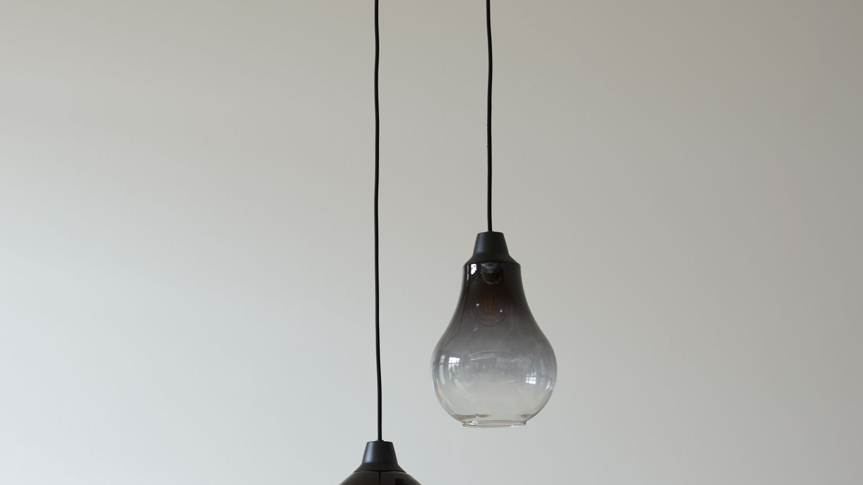Hängeleuchten mit schwarzen Glastropfenlampenschirmen Zwei Hängeleuchten mit tropfenförmigen Lampenschirmen aus schwarzem Glas an schwarzen Kabeln vor weißer Wand