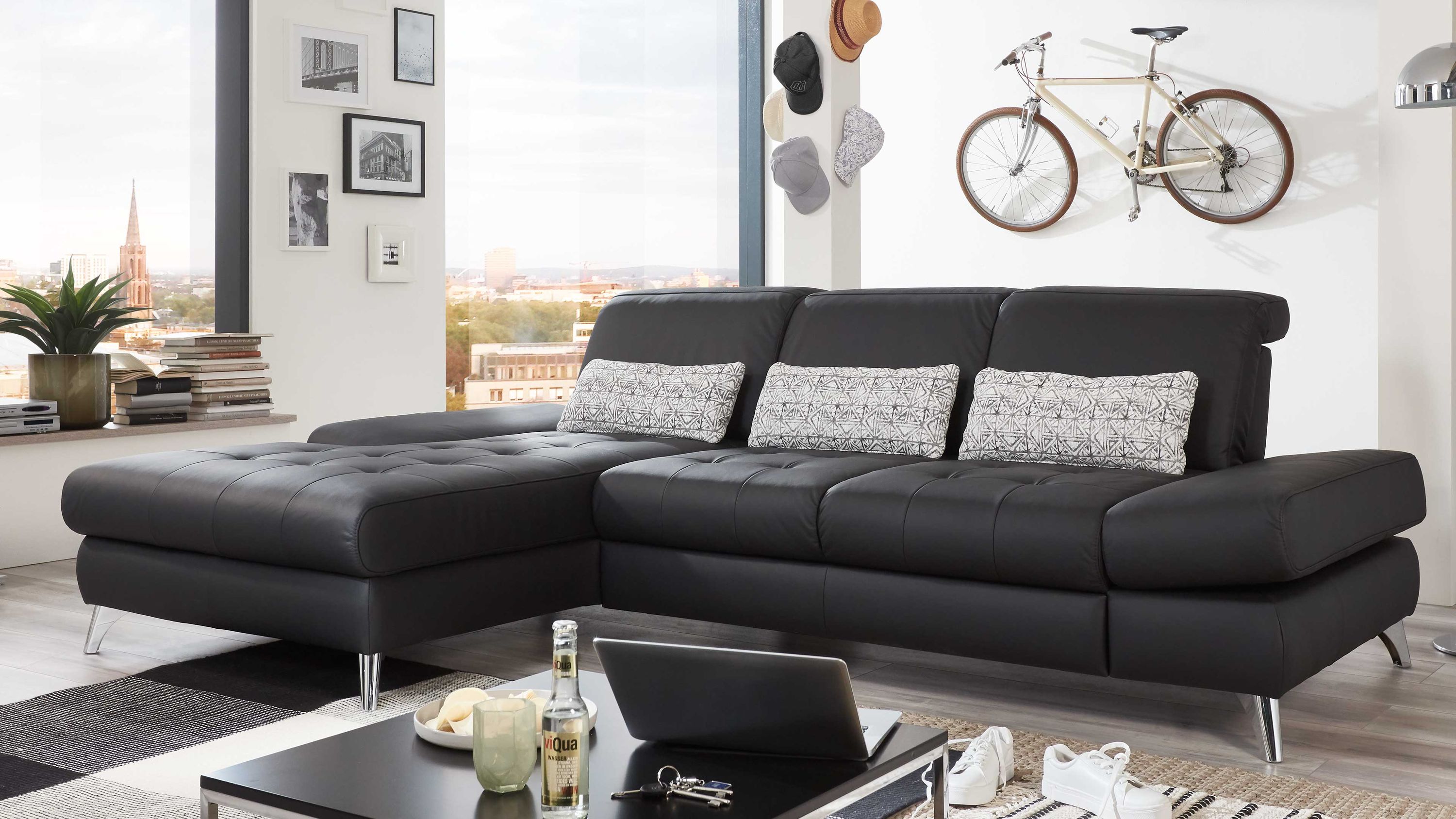 Ecksofa mit schwarzer Polsterung und Chromfüßen drei gemusterte Kissen moderner Wohnraum mit Fenster