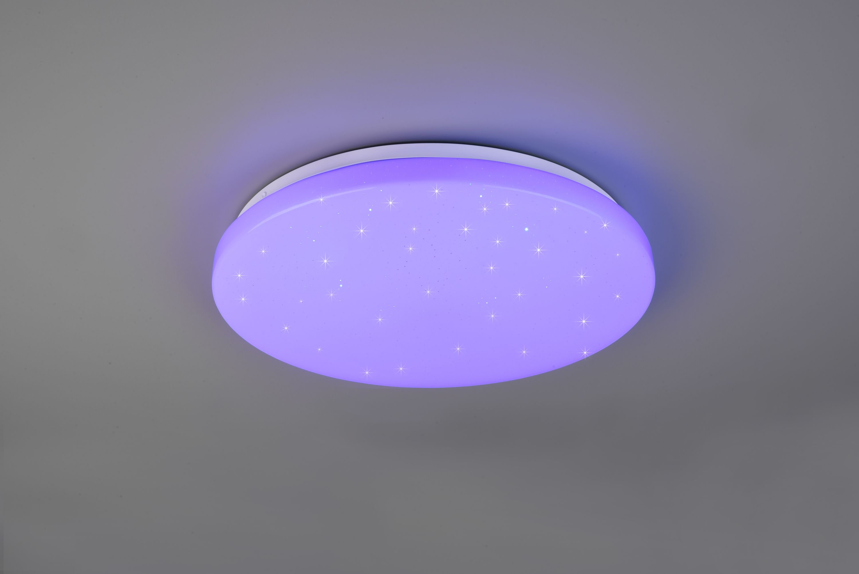 Runde Deckenleuchte aus weißem Kunststoff mit flachem Design  leuchtet violett; leicht schräg von unten fotografiert