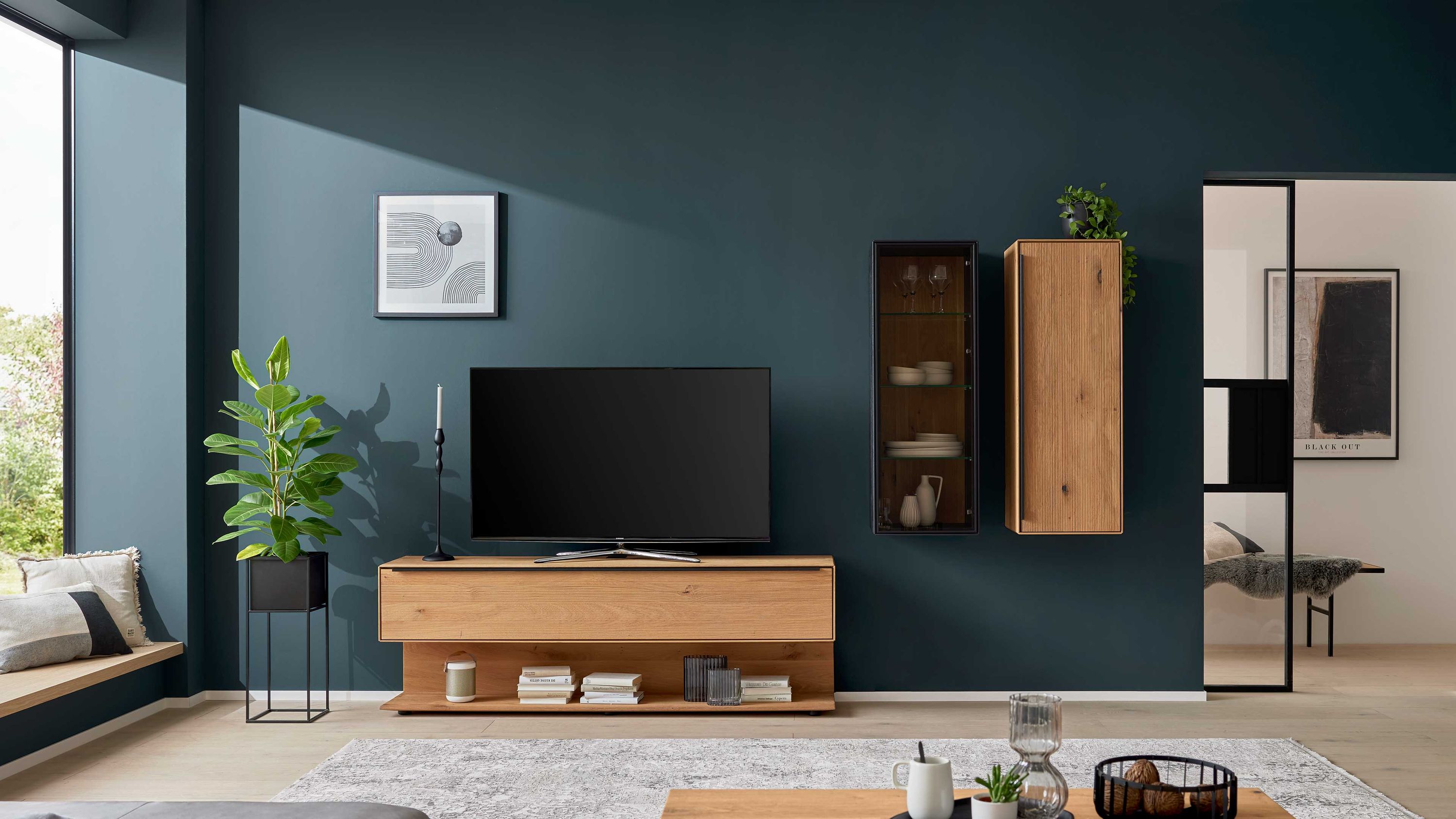 Dreiteilige Wohnwand aus hellem Holz an dunkelblauer Wand Dreiteilige Wohnwand aus hellem Holz mit TV-Board und zwei Hängeschränken an dunkelblauer Wand