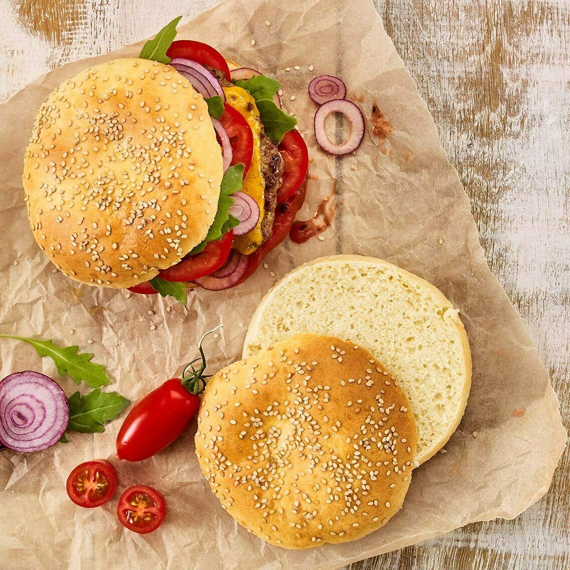 Draufsicht auf zwei belegte und zwei aufgeschnittene Burgerbrötchen auf Backpapier mit Gemüse  rustikal angerichtet