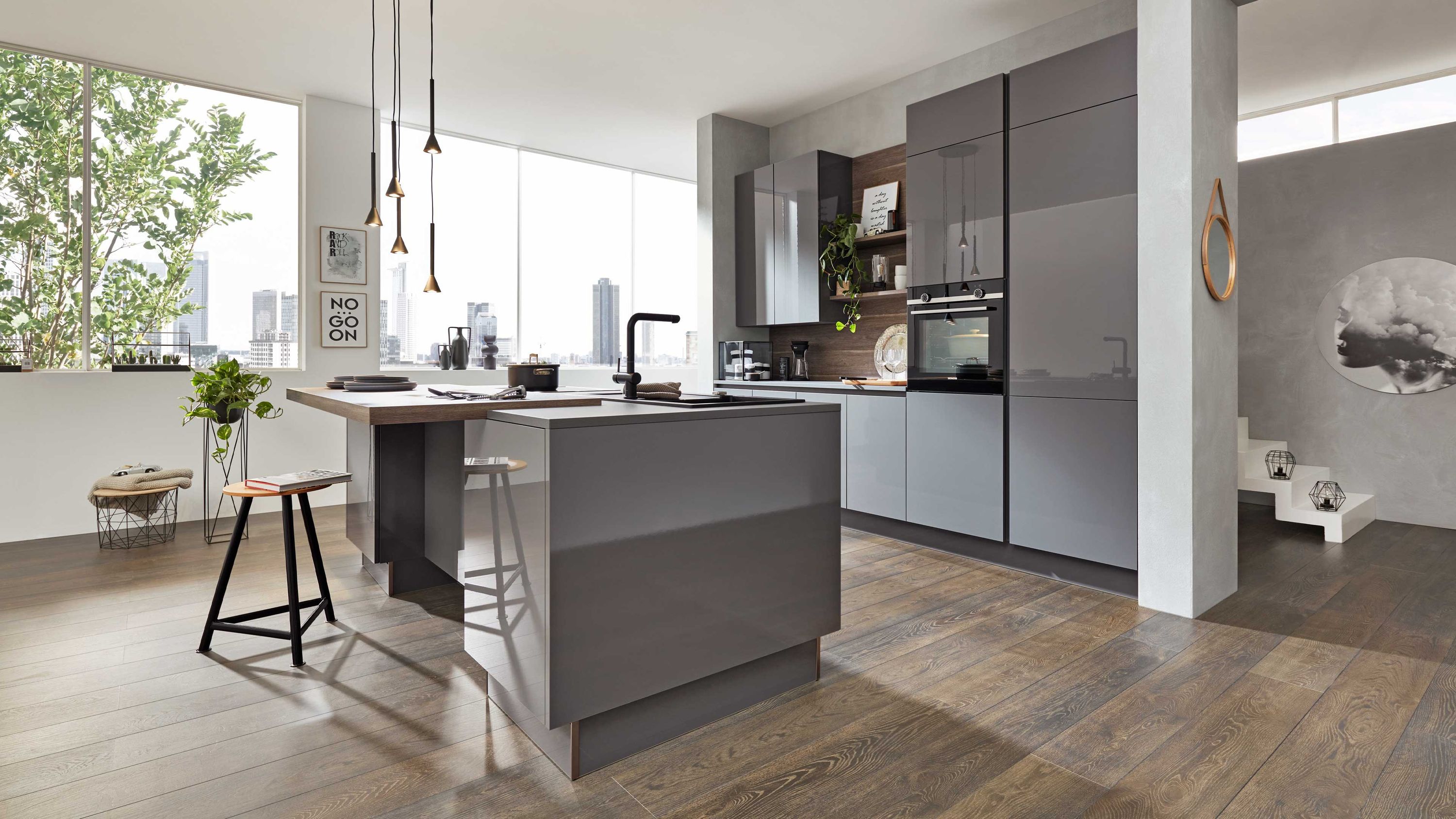 Moderne Küche mit Naturblick klarer Linienführung und wohnlichem Materialmix Graue Küche mit Insel Hängelampen Barhockern Fensterlicht Einbaugeräten Holzfußboden Blick ins Grüne