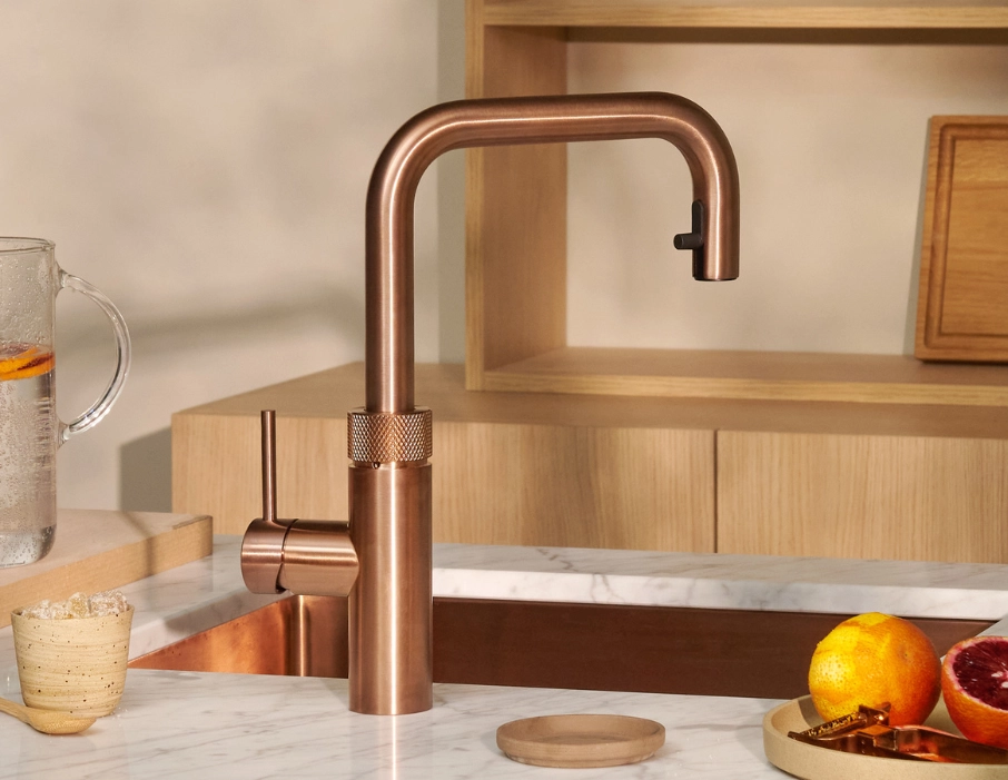 Moderne Küche mit Kupferarmatur, integrierter Spüle in Marmorarbeitsplatte, Holzfronten und dekorativen Zitrusfrüchten.