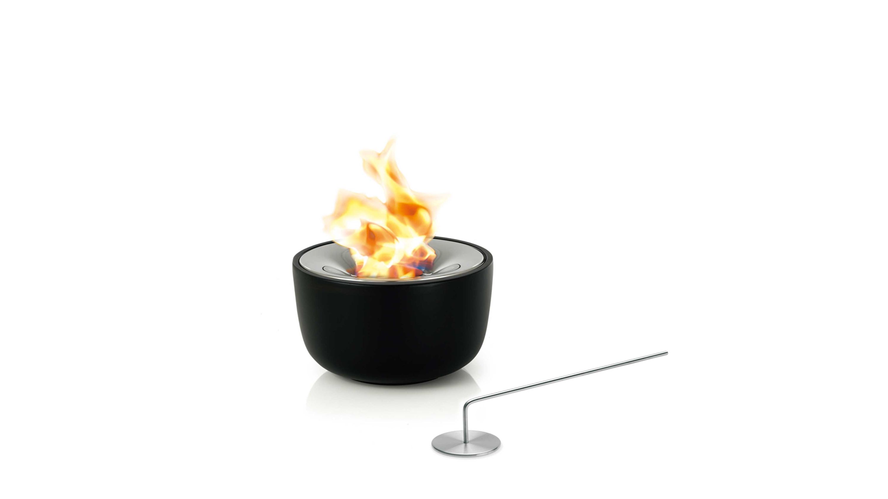 Runde schwarze Feuerstelle mit poliertem Edelstahlrand und brennender Flamme daneben ein langer Metallstab