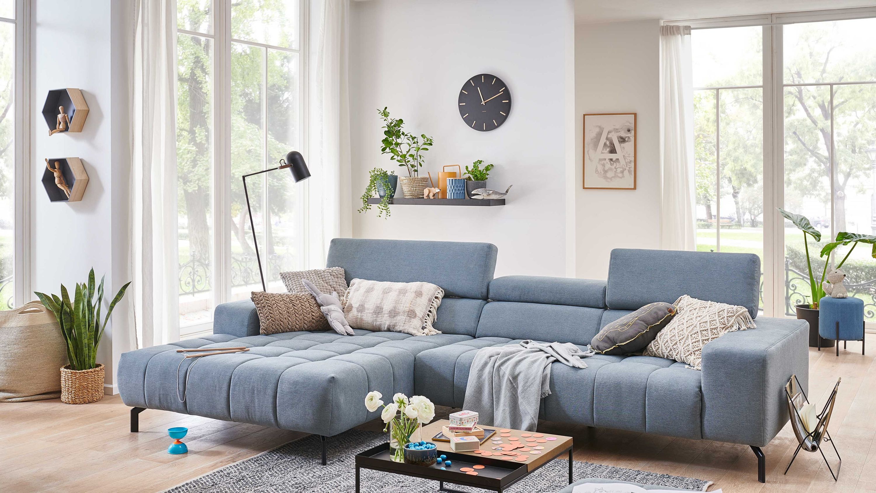 Ecksofa mit stahlfarbenem Stoffbezug und schwarzen Metallfüßen mit Kissen und Decke dekoriert
