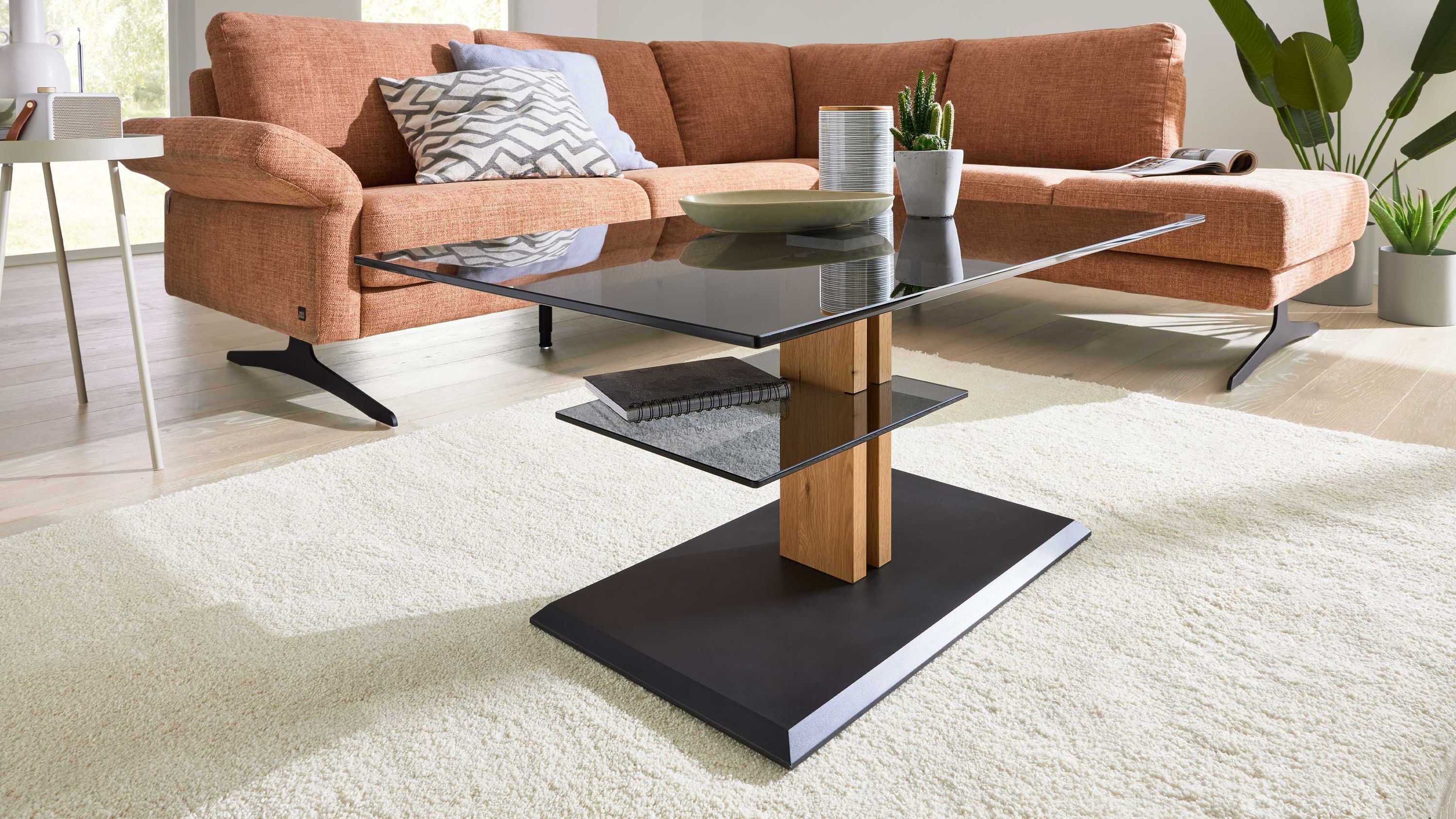 Rechteckiger Couchtisch mit grauer Glasplatte Holzsäule und schwarzer Basis vor orangefarbenem Sofa