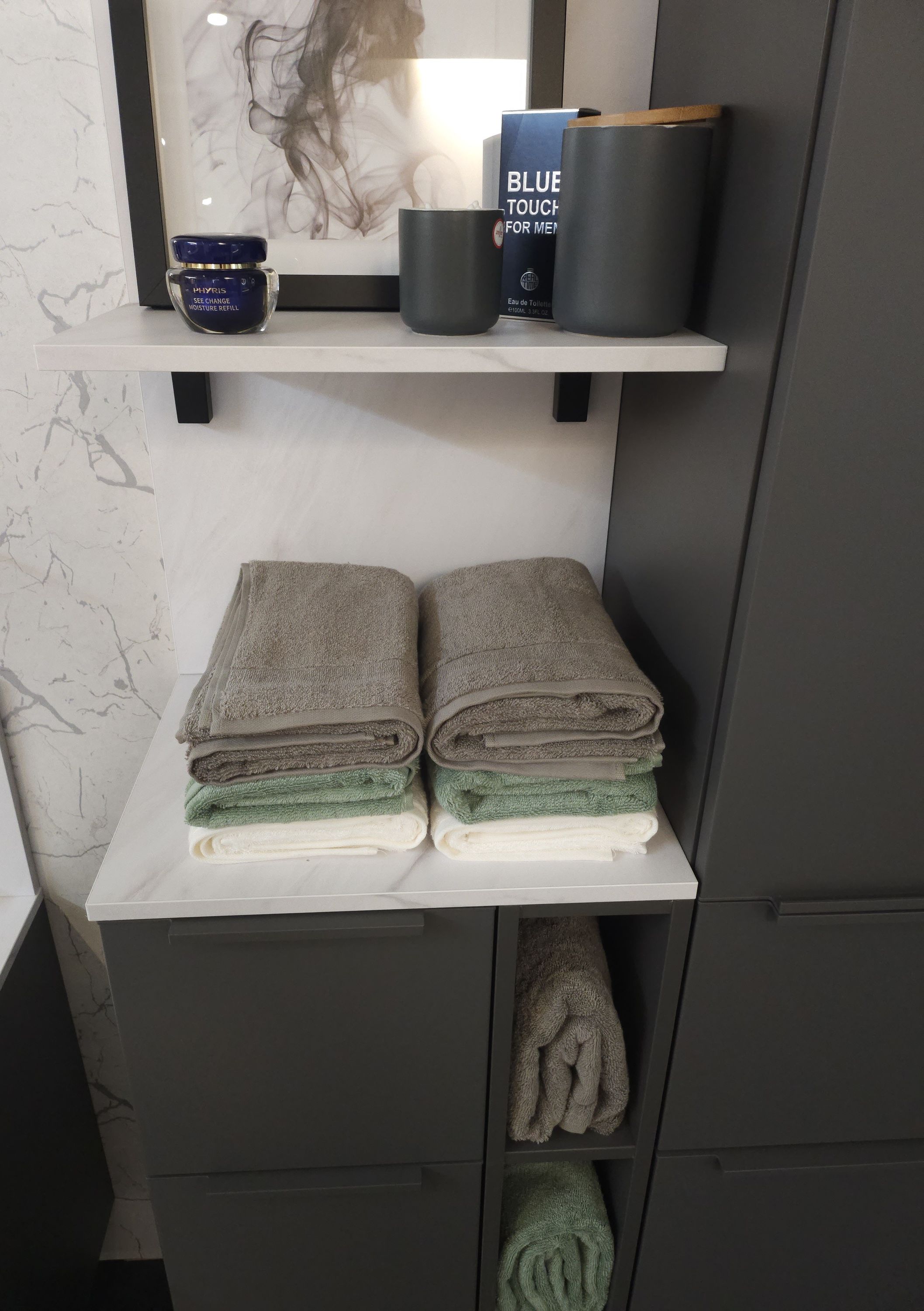 Badezimmerregal frontal mit grauen Handtüchern Bild blauem Behälter und zwei Dosen auf oberem Brett