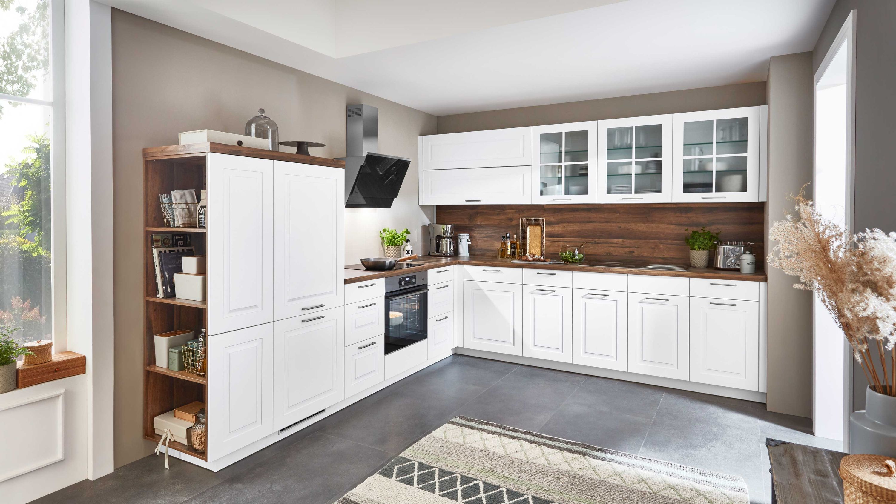 Landhaus-Winkelküche in Weiß mit Holzarbeitsplatte. Weiße Winkelküche im Landhausstil mit Glashängeschränken Holzarbeitsplatte Regal und Einbaugeräten.