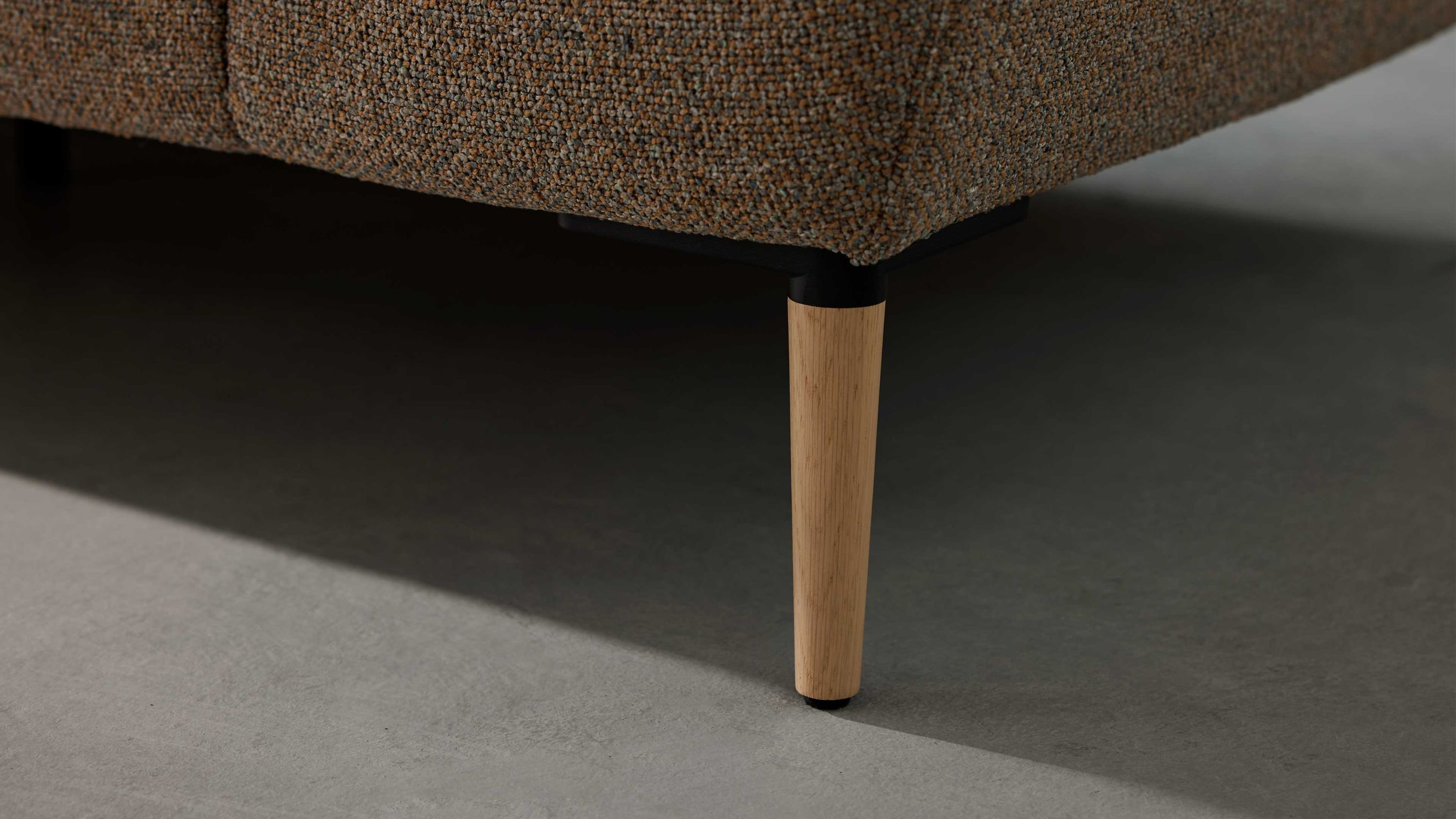 Runder Holzfuß in heller Farbe unter einem braunen Sofa