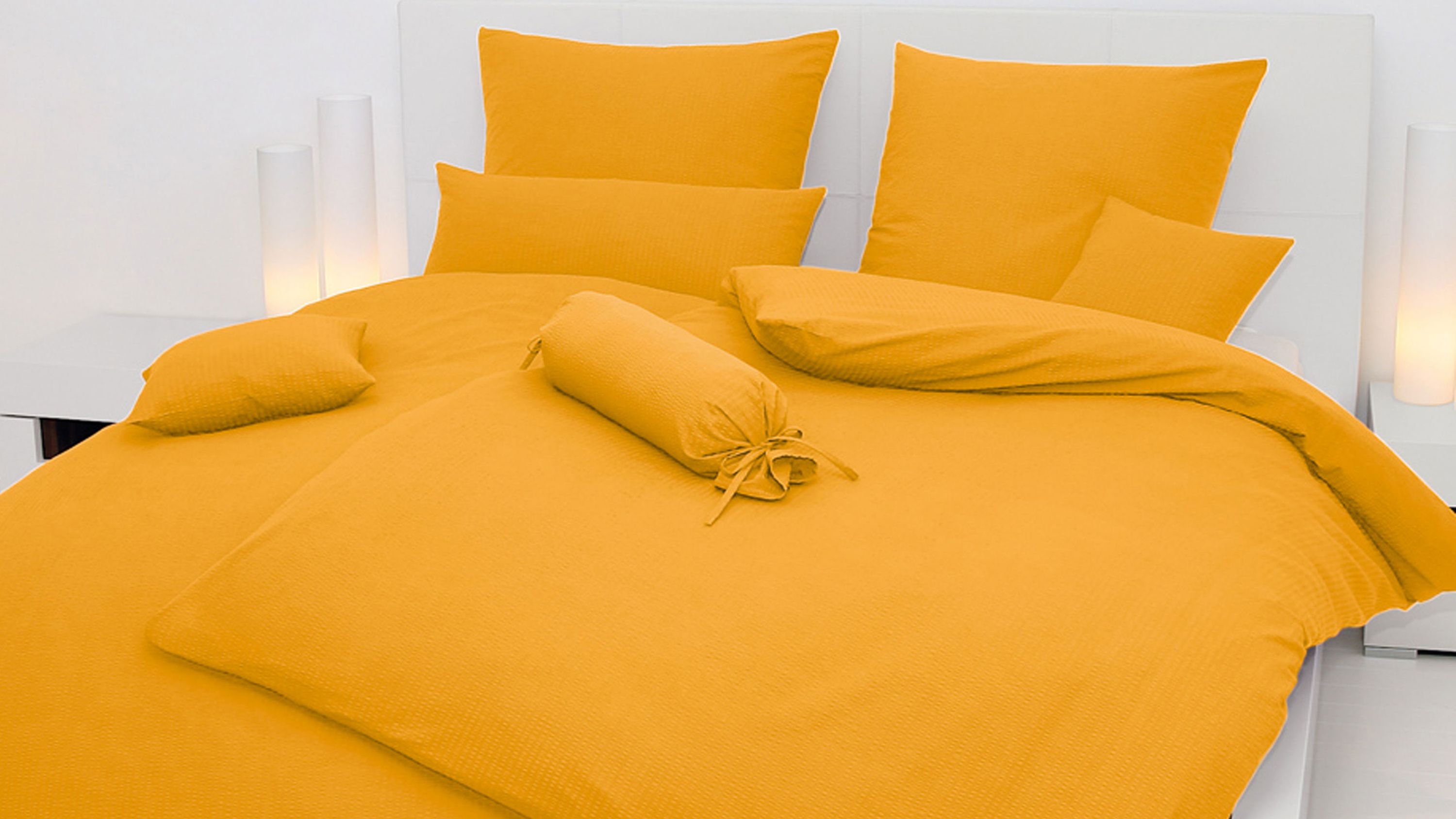 Gelbes Bettwäsche-Set mit Kissen und Zierkissen auf weißem Bett mit Kopfteil