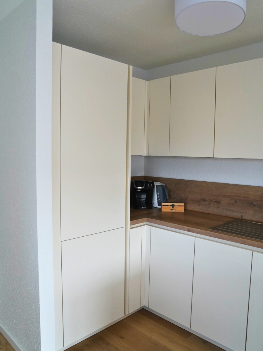 Helle L-Küche mit Kochinsel, Holzarbeitsplatte, weißen Fronten, Induktionskochfeld und Dekoration auf Parkettboden.