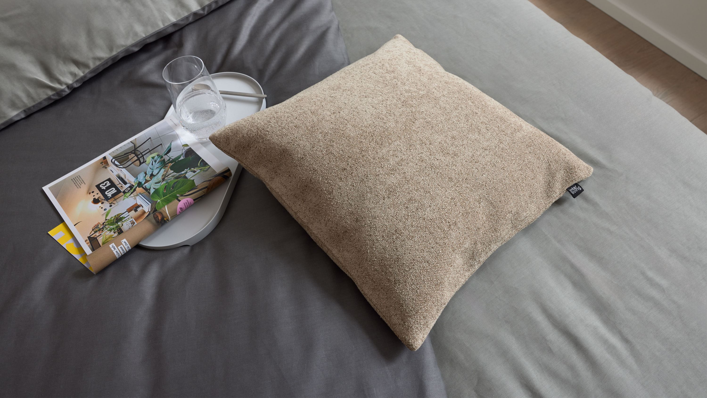 Beiges quadratisches Kissen auf Bett Beige quadratisches Kissen mit strukturierter Oberfläche auf grauem Bettbezug