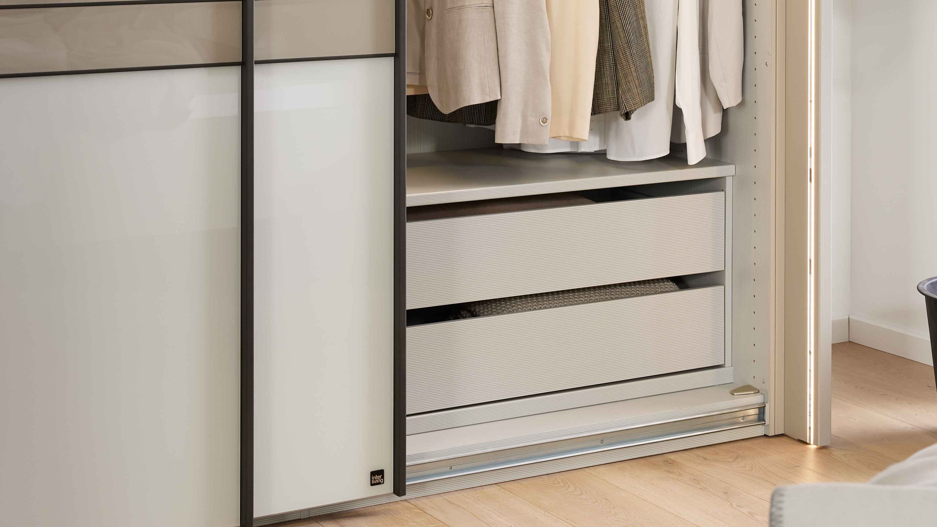 Offener Kleiderschrank mit zwei weißen Innenschubladen und hängender Kleidung