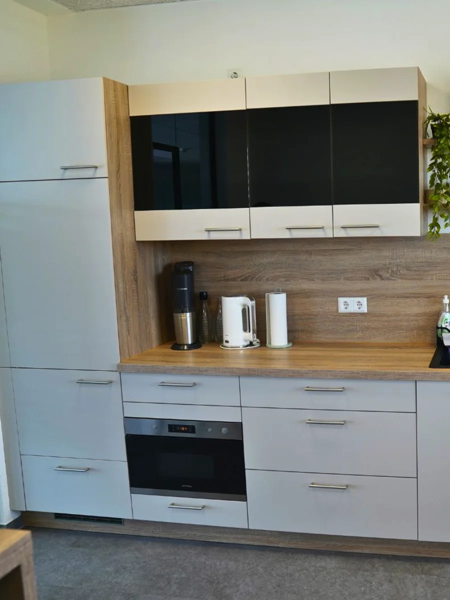 Moderne Küchenzeile mit grauen Fronten, Holzarbeitsplatte, schwarzer Spüle, Einbaugeräten, offenen Regalen und Kaffeemaschine.