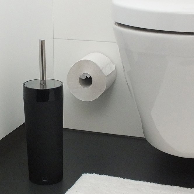 Badezimmer-Essentials Schwarzer WC-Bürstenhalter neben weißer Toilette mit montierter Toilettenpapierrolle, frontal aufgenommen.
