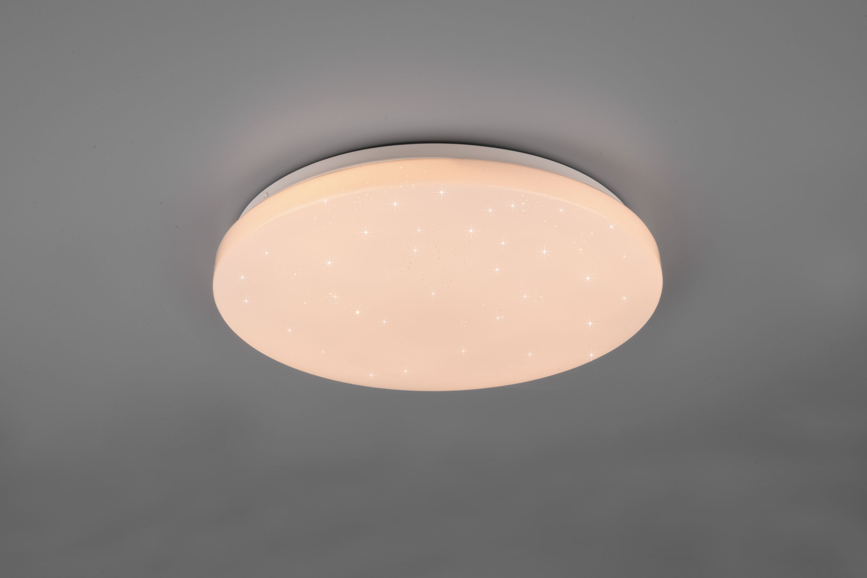 Runde Deckenleuchte aus weißem Kunststoff mit flachem Design  leuchtet warmweiß; leicht schräg von unten fotografiert