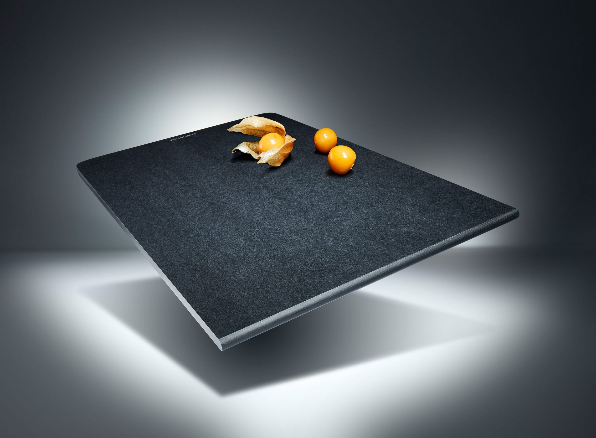 Schwarzes Schneidebrett  schwebend inszeniert mit Orangenschalen und Knoblauch auf dunklem Hintergrund