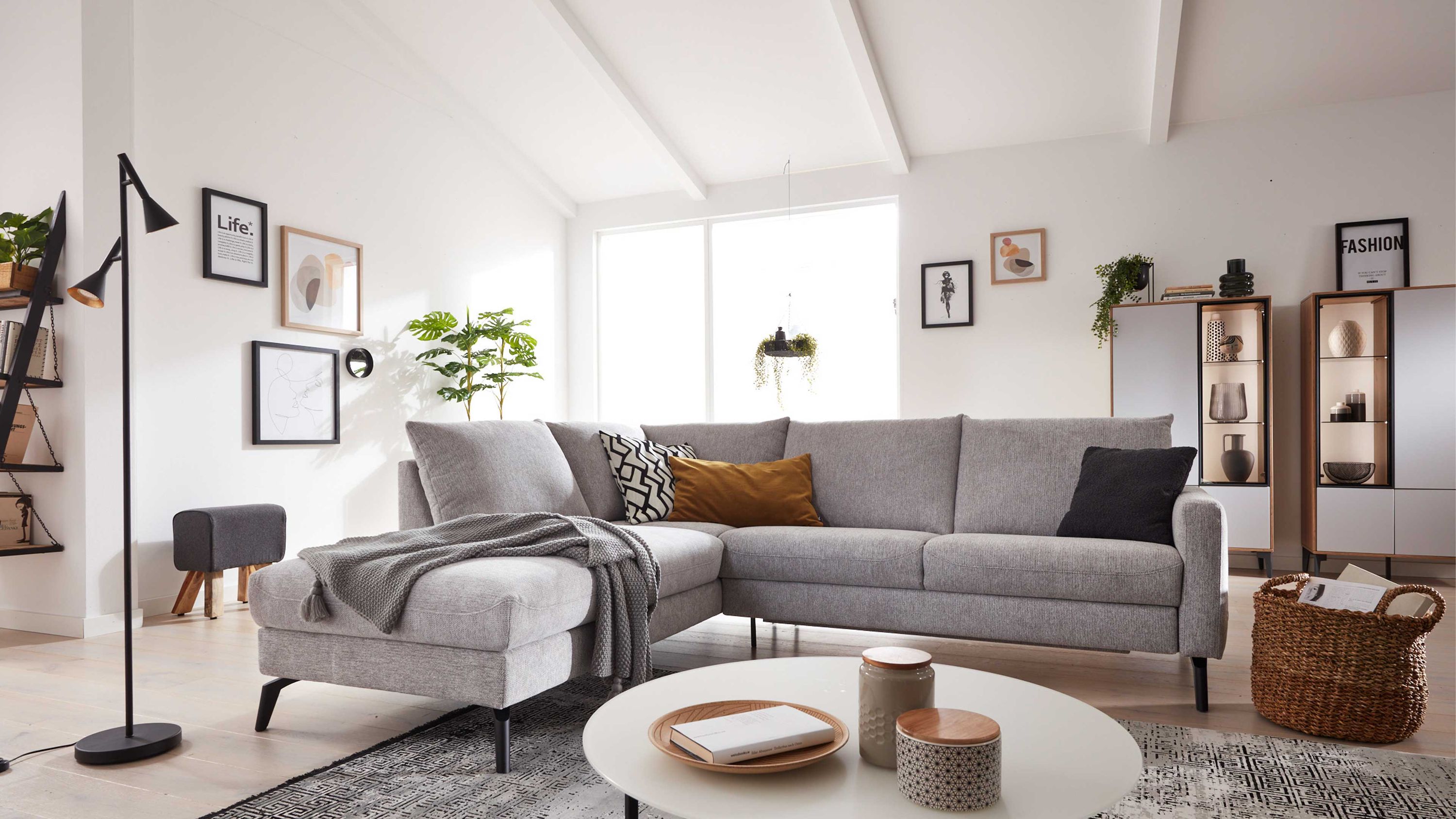 Ecksofa mit steingrauem Bezug und schwarzen Füßen in modernem Wohnzimmer mit Kissen und Decke