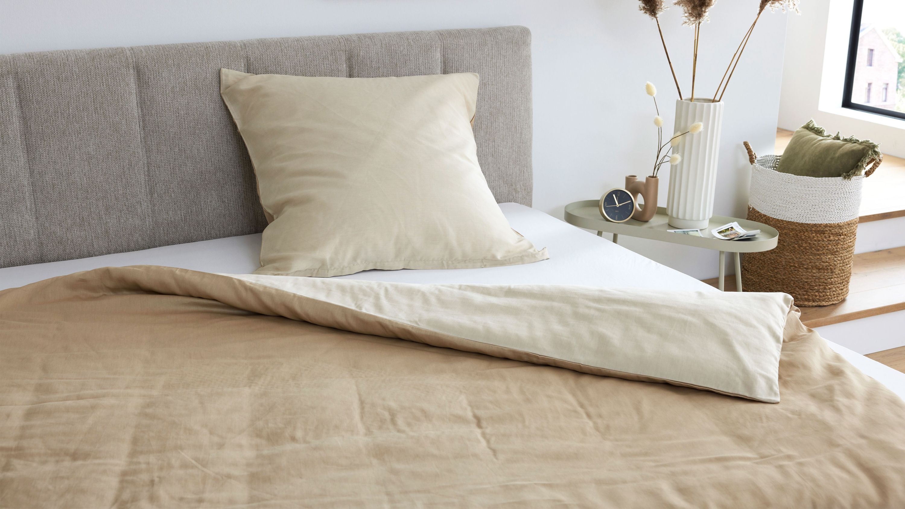 Sandfarbene Bettwäsche aus Baumwollsatin auf einem Bett mit grauem gepolstertem Kopfteil