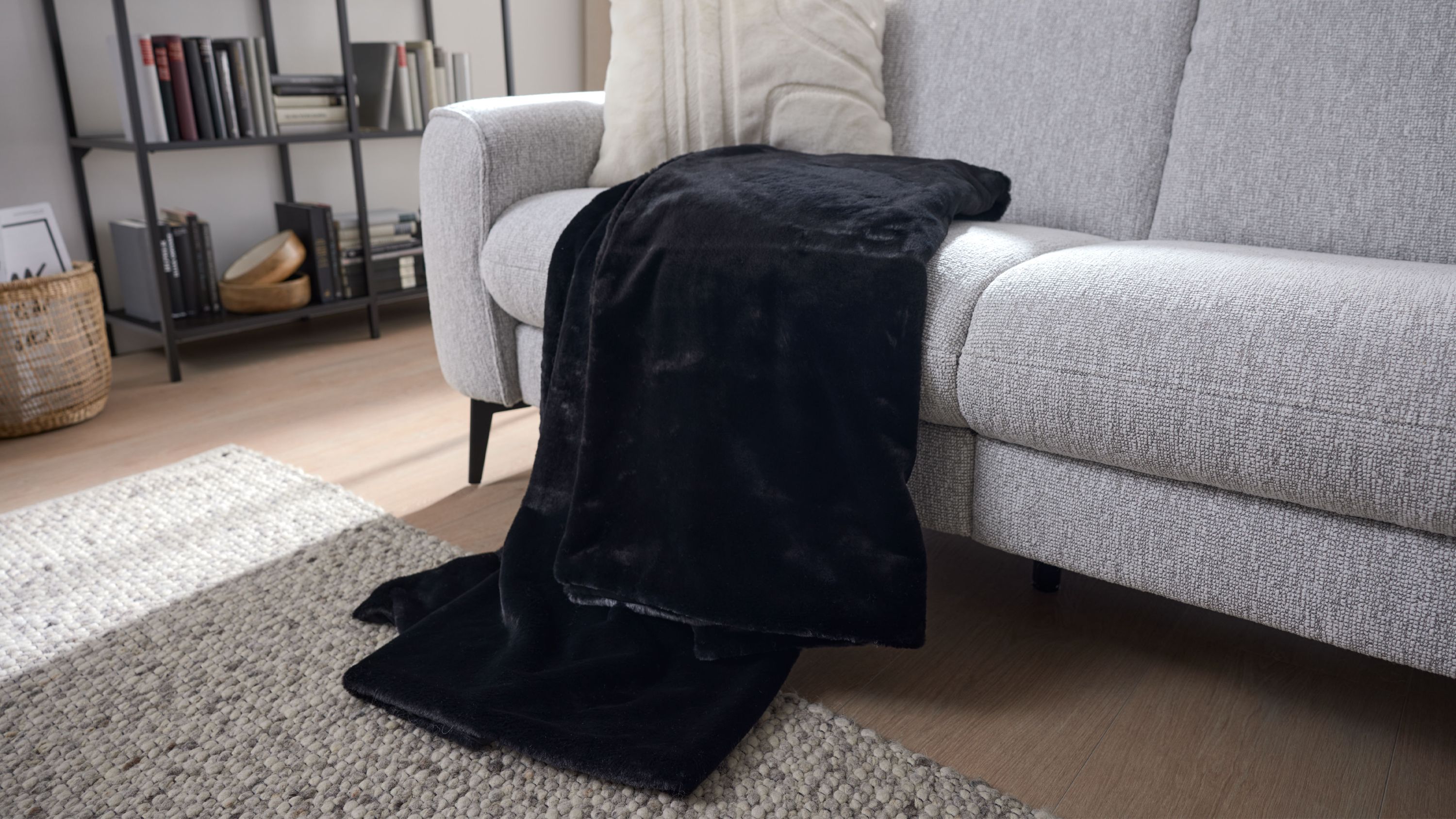 Schwarze Wohndecke aus Kunstfell liegt auf einem hellgrauen Sofa in einem Wohnzimmer