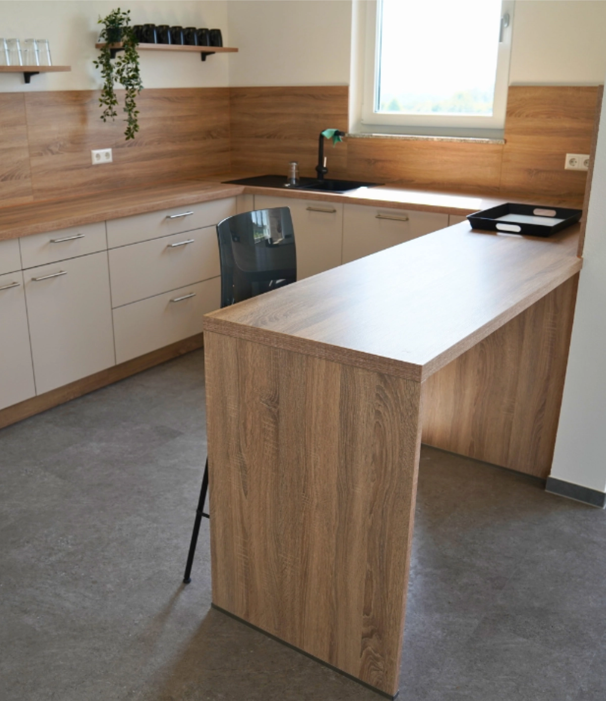 Moderne Büroküche mit Holzfronten, Arbeitsinsel, Hochschränken, Spüle und Fenster, funktionaler Pausen‑ und Aufenthaltsbereich im Büro