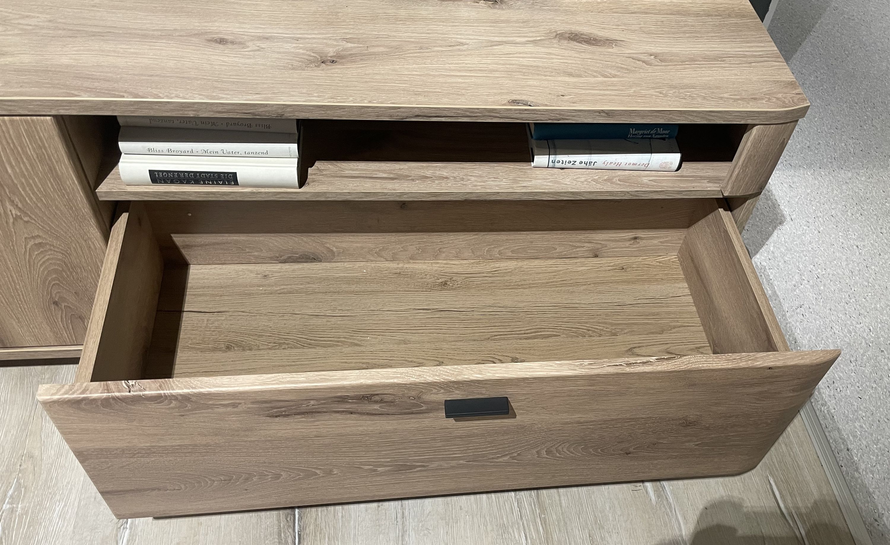 Offene Schublade und Ablagefach einer hellbraunen Wohnwand mit Holzstruktur