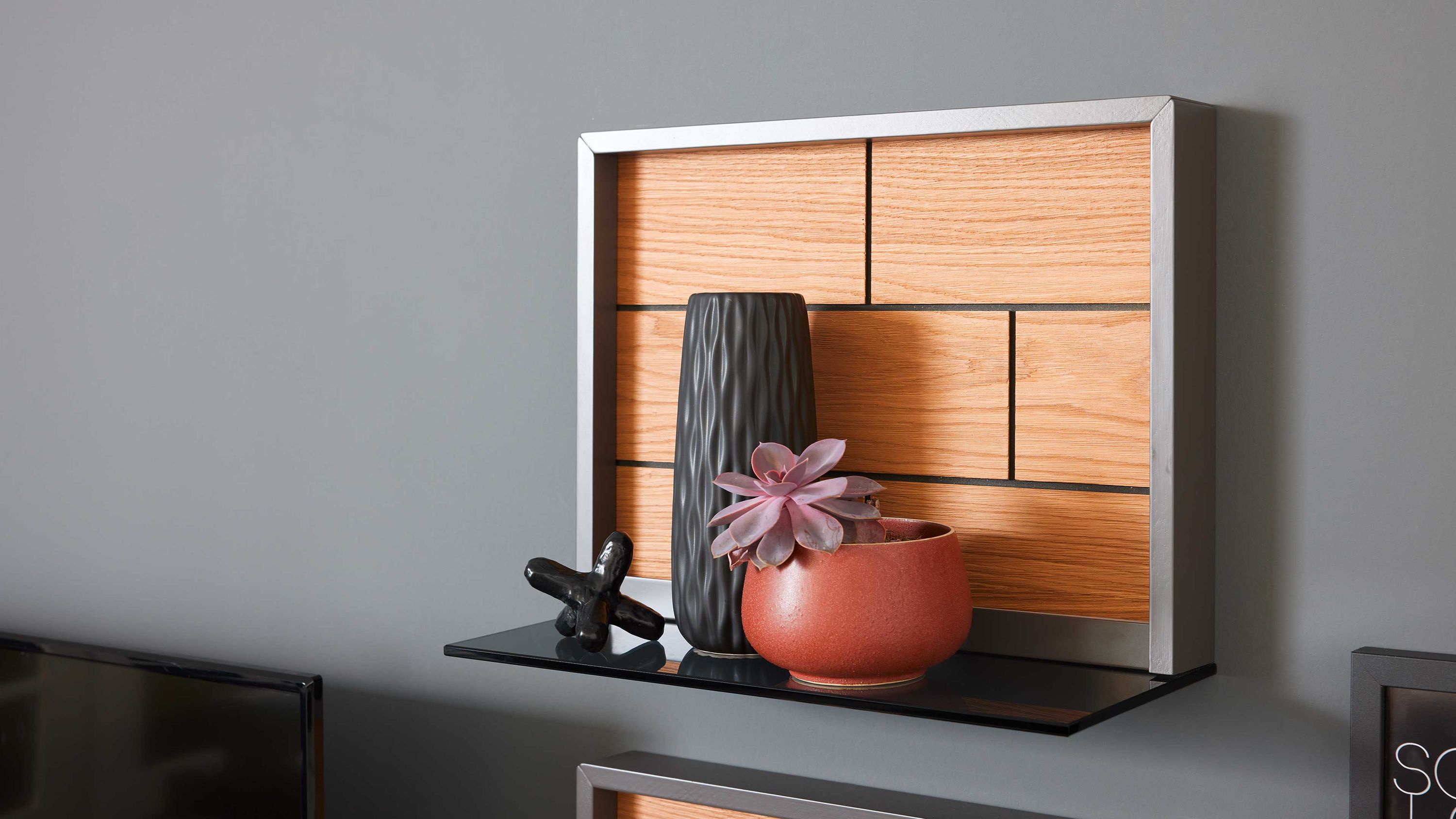 Wandboard mit Holzrücken und schwarzer Ablagefläche Rechteckiges Wandboard mit schwarzer Ablagefläche und hellbraunem Holzrücken an grauer Wand mit Dekoration