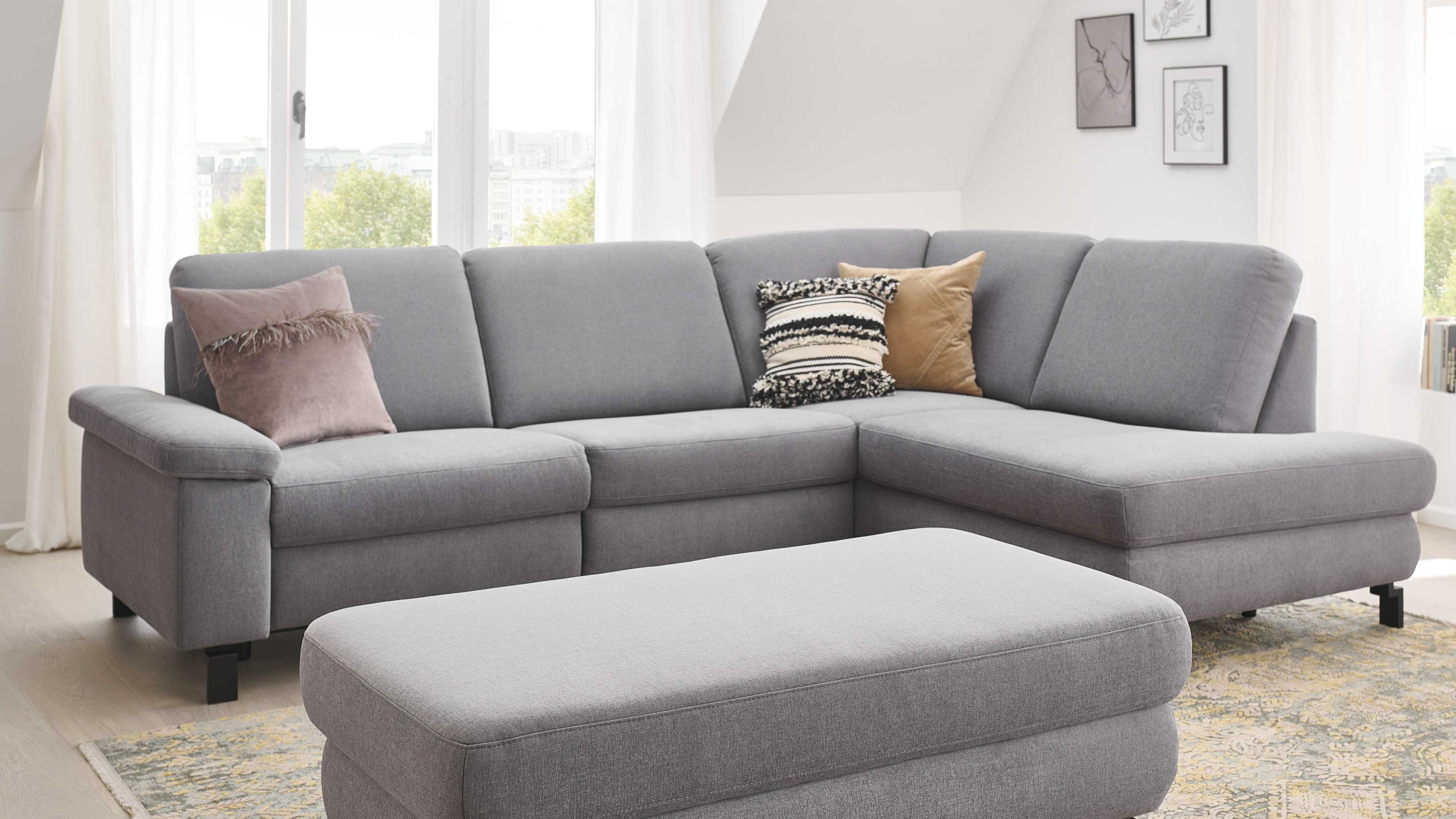 Ecksofa mit platingrauem Bezug und schwarzen Metallfüßen dazu ein passender Hocker in gleicher Farbe