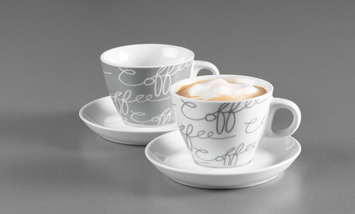 Zwei Cappuccinotassen mit Untertassen in Weiß und Grau mit Schriftzug auf grauem Hintergrund