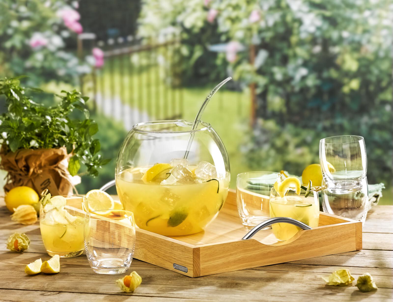 Bowle-Set mit runder Glasbowl, Schöpfkelle und Gläsern auf Holztablett, dekoriert mit Zitronen, Kräutern und Eiswürfeln