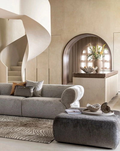 Wohnzimmer mit Wendeltreppe und stilvoller Einrichtung. Modernes Wohnzimmer mit grauem Sofa, gemustertem Teppich, runder Wendeltreppe und dekorierter Kücheninsel im Hintergrund.