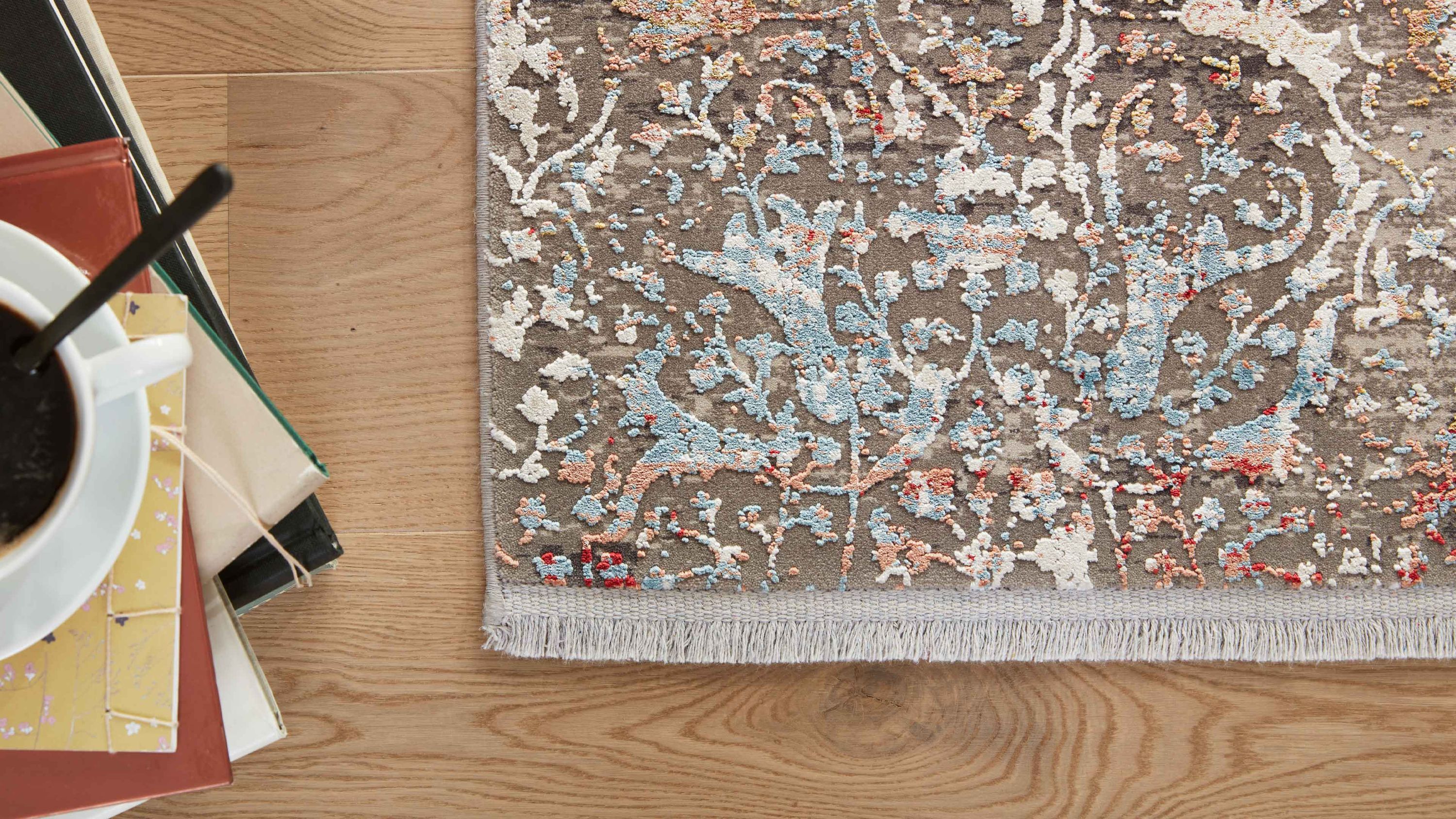 Teppich mit floralem Muster in grau blau rot und beige mit Fransen auf hellem Holzboden