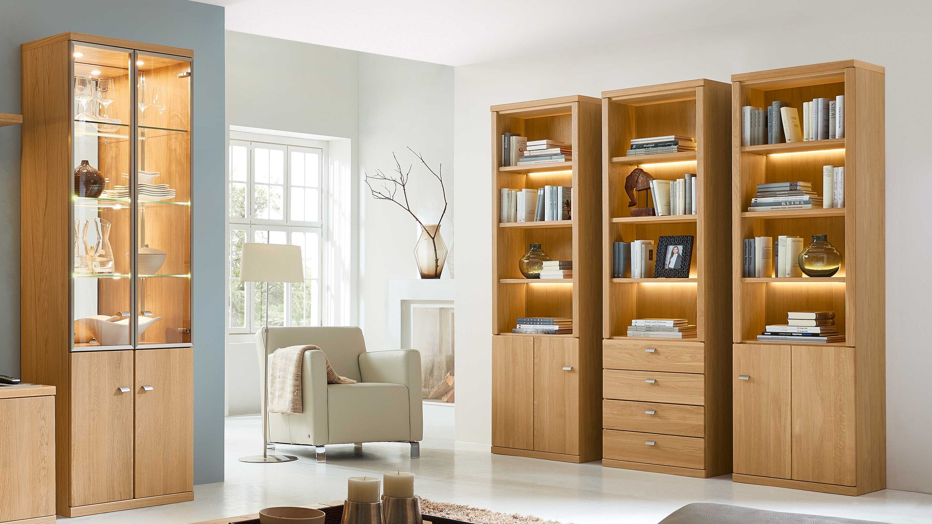 Hohe Holzregale mit Beleuchtung und Stauraum Drei hohe Holzregale mit offenen und geschlossenen Fächern beleuchtet mit Büchern und Dekoration