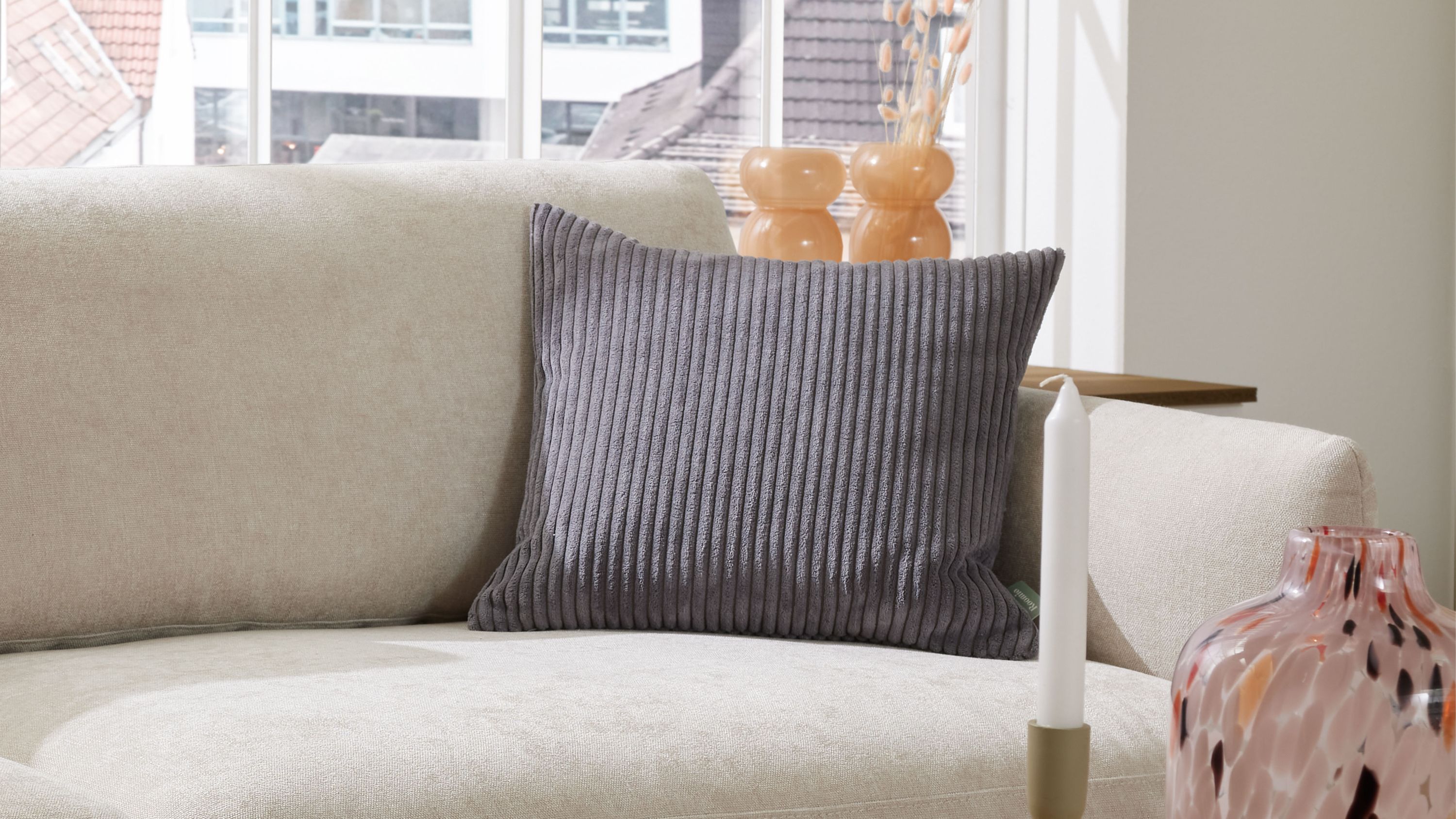 Kissen mit breitem grauem Cordmuster auf Sofa Rechteckiges Kissen mit breiten grauen Cordstreifen auf hellem Sofa vor Fenster