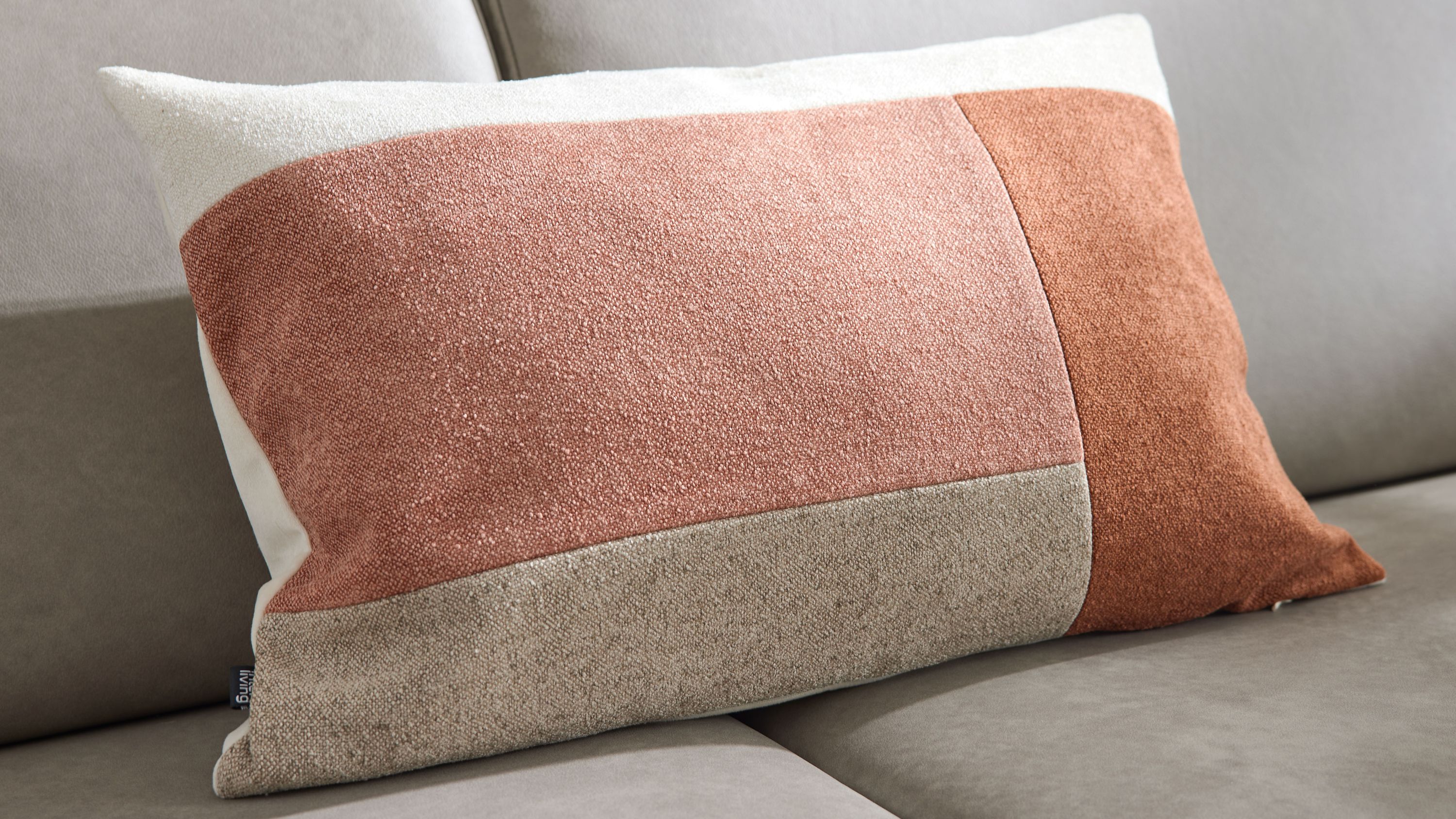 Rechteckiges Kissen mit farbigen Stoffflächen in Sand- und Rosatönen auf grauem Sofa