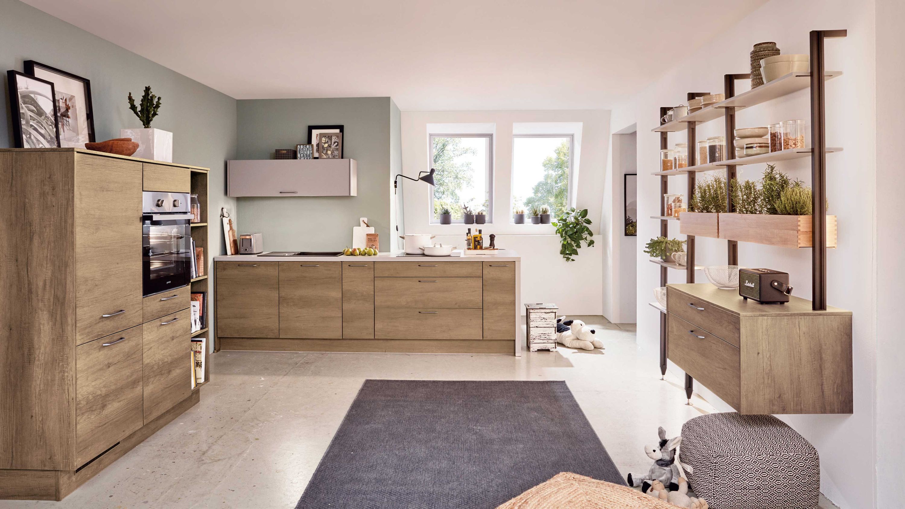 Küche in Holzoptik mit grauer Arbeitsplatte Einbauofen offenen Regalen und heller Raumgestaltung mit Fenstern.