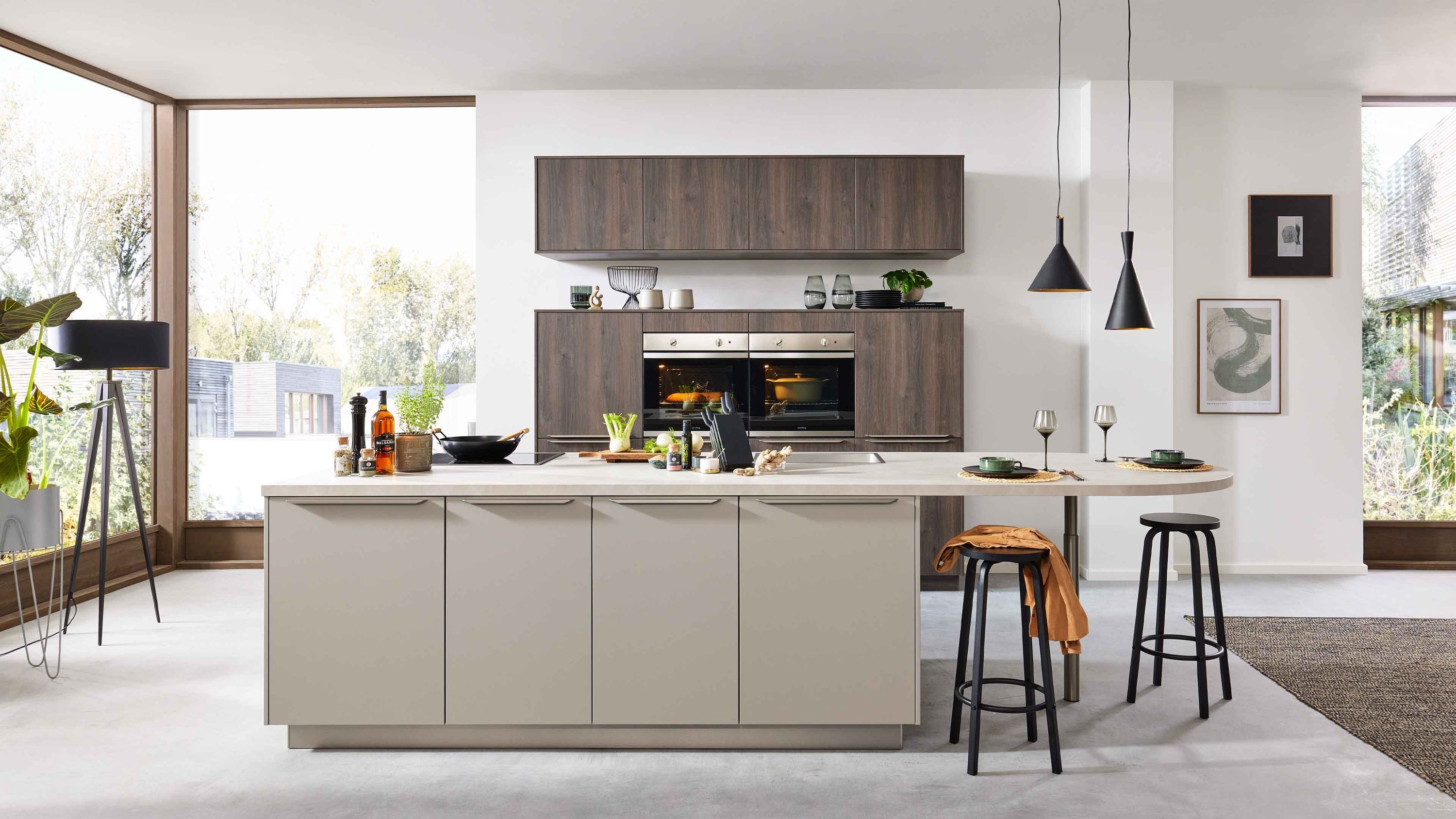 Moderne Inselküche in Beige mit Holzfronten Hängeschränken Einbaugeräten und schwarzen Pendelleuchten.