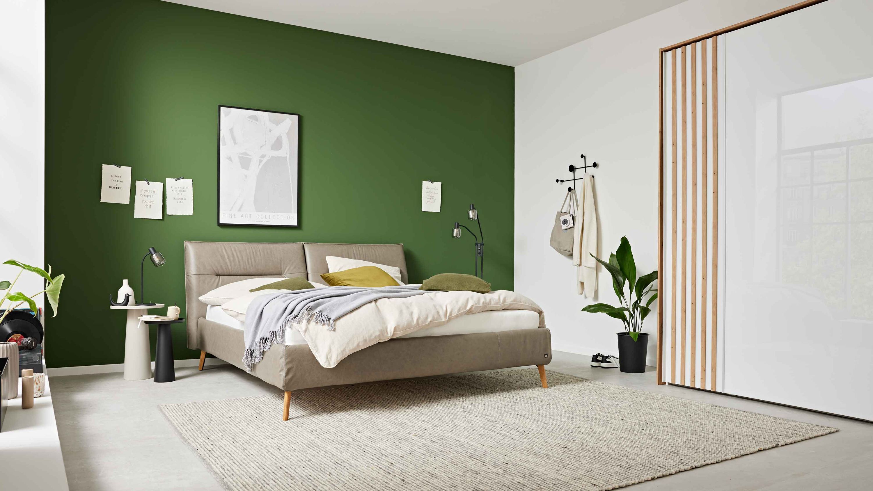 Polsterbett mit gepolstertem Kopfteil und hellbraunem Bezug Holzfüße vor grüner Wand in modernem Schlafzimmer