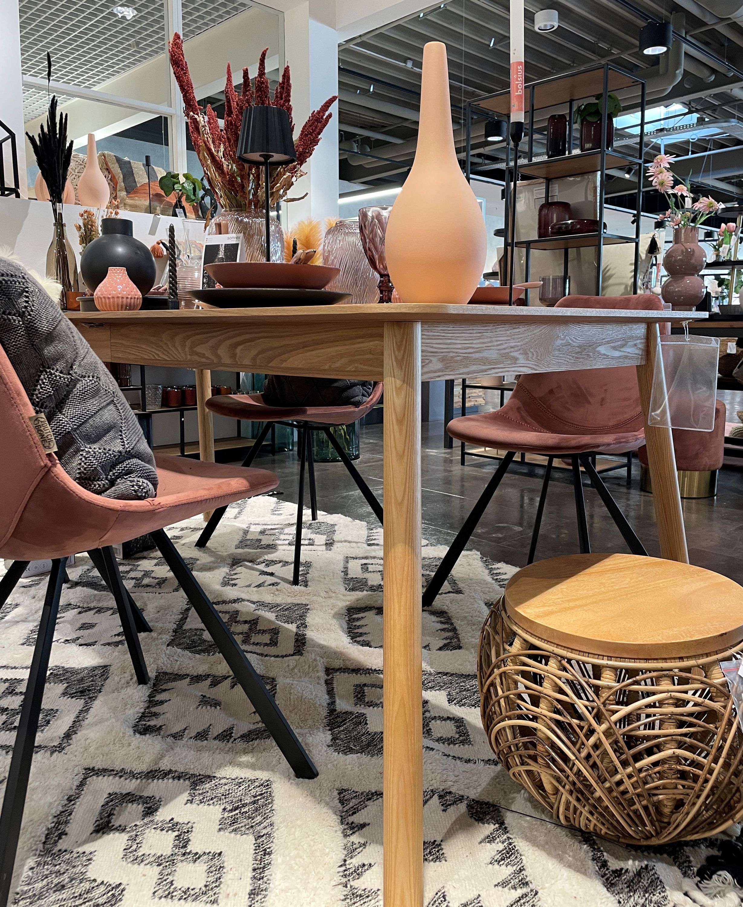 Seitliche Ansicht eines Holztisches mit rosa Stühlen, dekoriert mit hoher beigefarbener Vase, Tellern und Gläsern auf gemustertem Teppich.