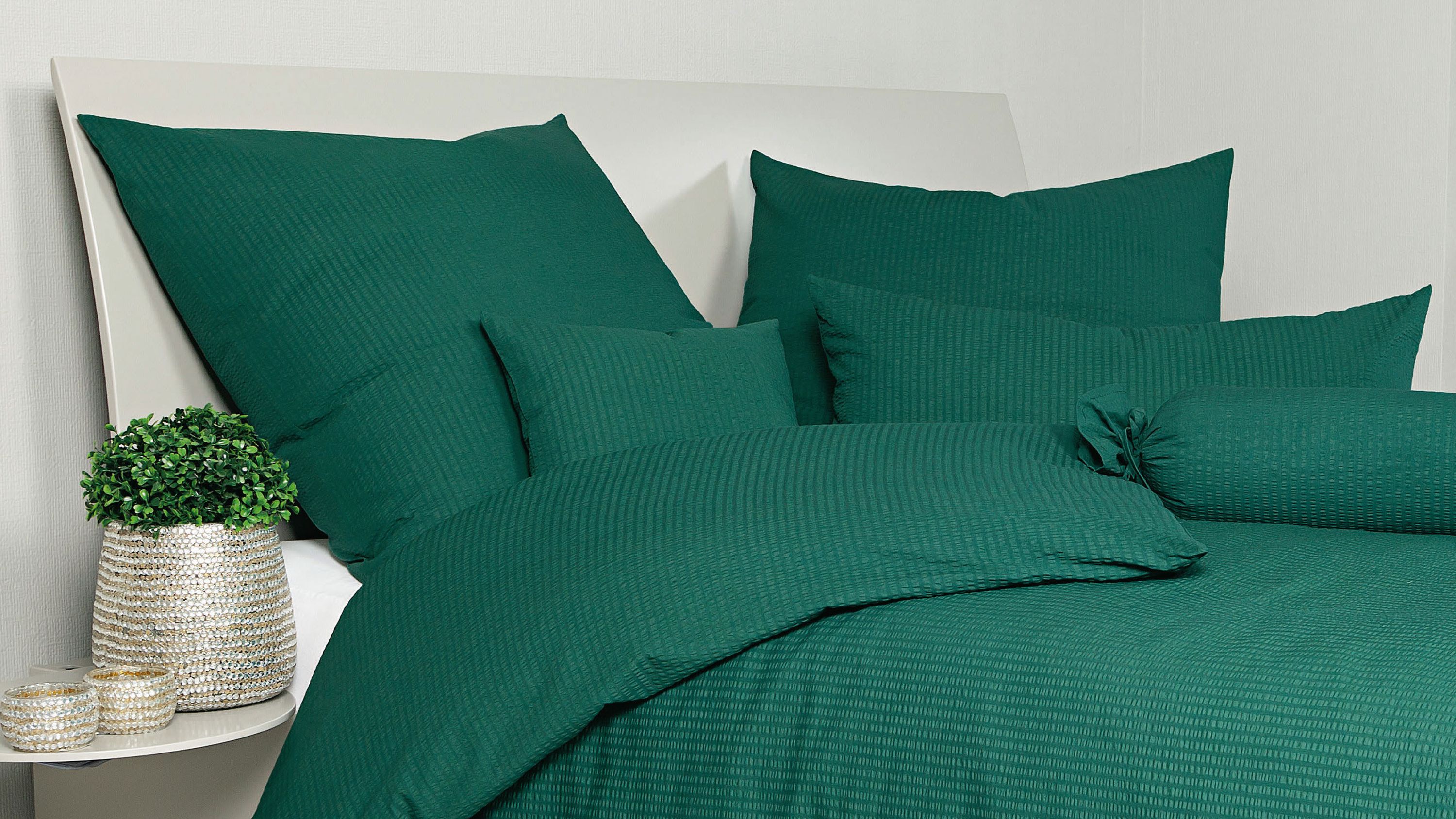 Bett mit waldgrüner Bettwäsche bestehend aus Kissen und Decke mit feiner Struktur