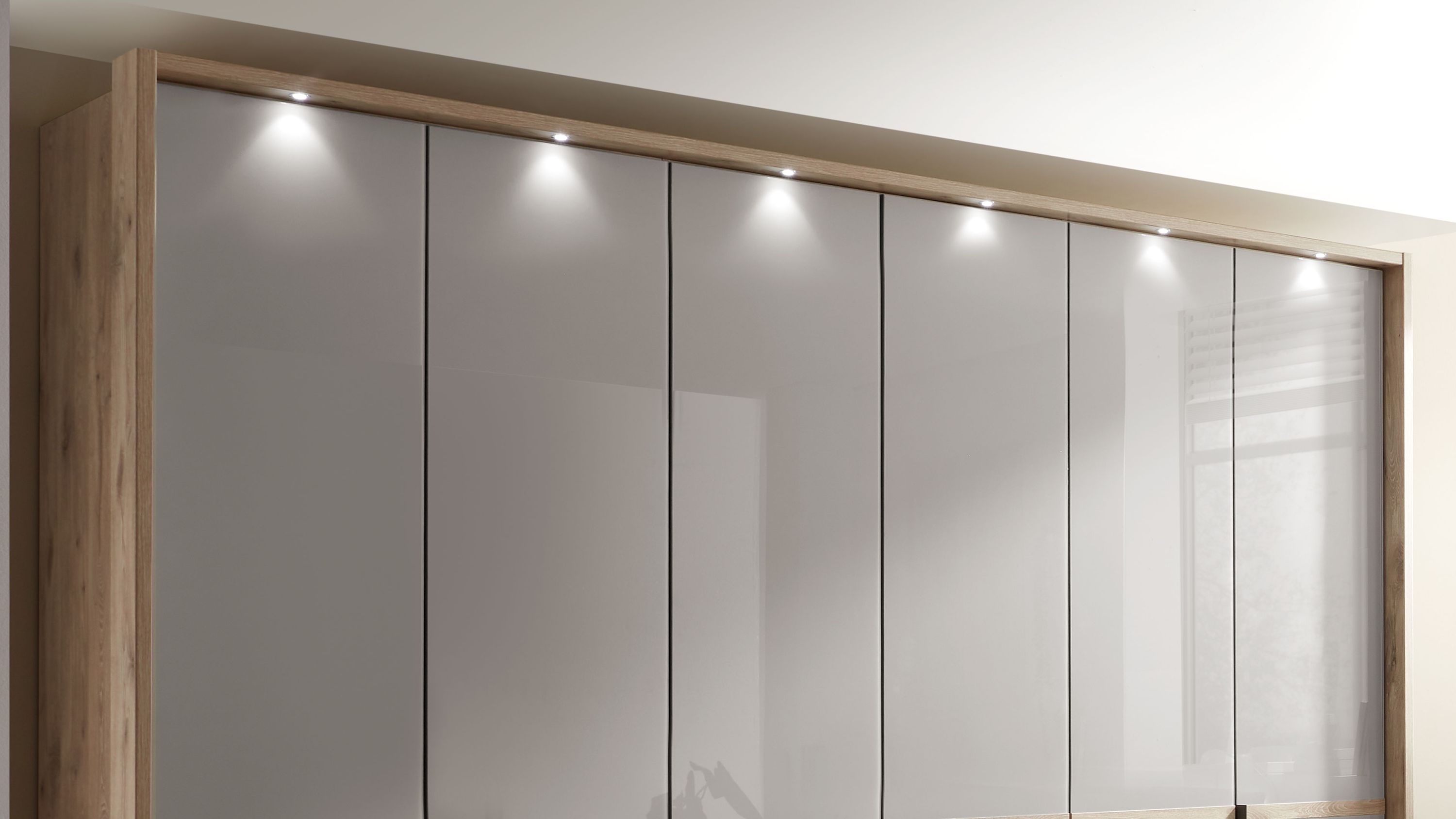 Großer Kleiderschrank mit sechs glatten weißen Türen und Holzrahmen in heller Eiche mit integrierten Deckenleuchten