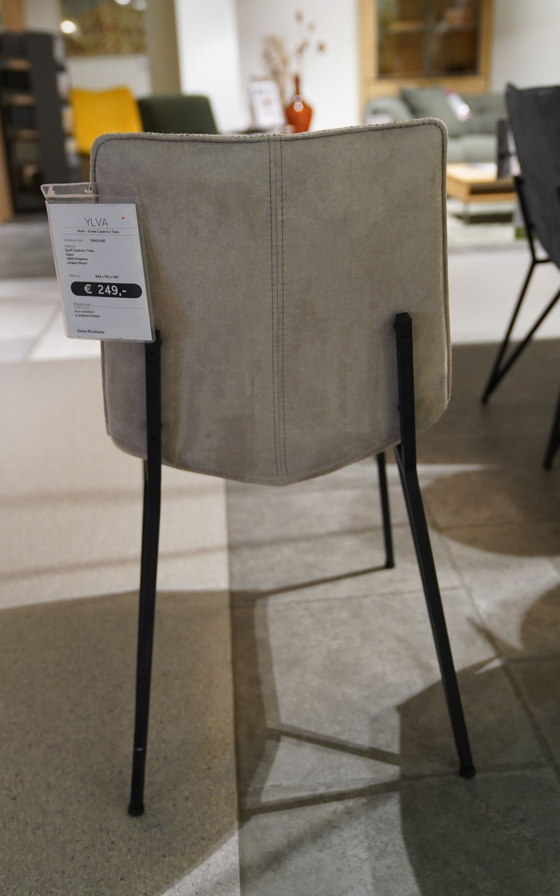 Rückansicht des Stuhls Ylva mit grauem Microfaserbezug und schwarzen Metallbeinen, Preisschild sichtbar.