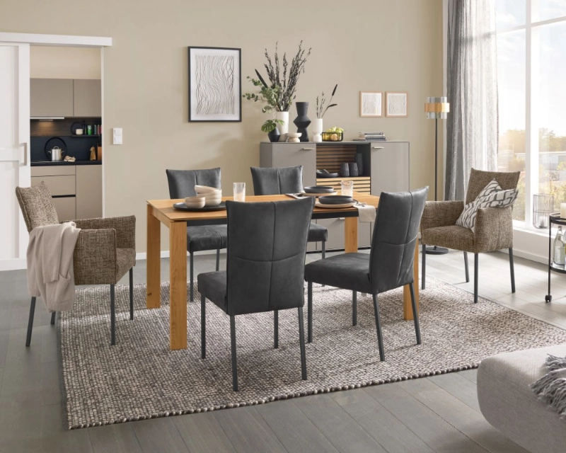 Zeitloses Esszimmer mit Massivholztisch, grauen Stühlen und wohnlicher Dekoration auf gemütlichem Teppich. Essgruppe mit Massivholztisch, gepolsterten Stühlen in Grau und Dekoration auf Teppich in modernem Wohnambiente